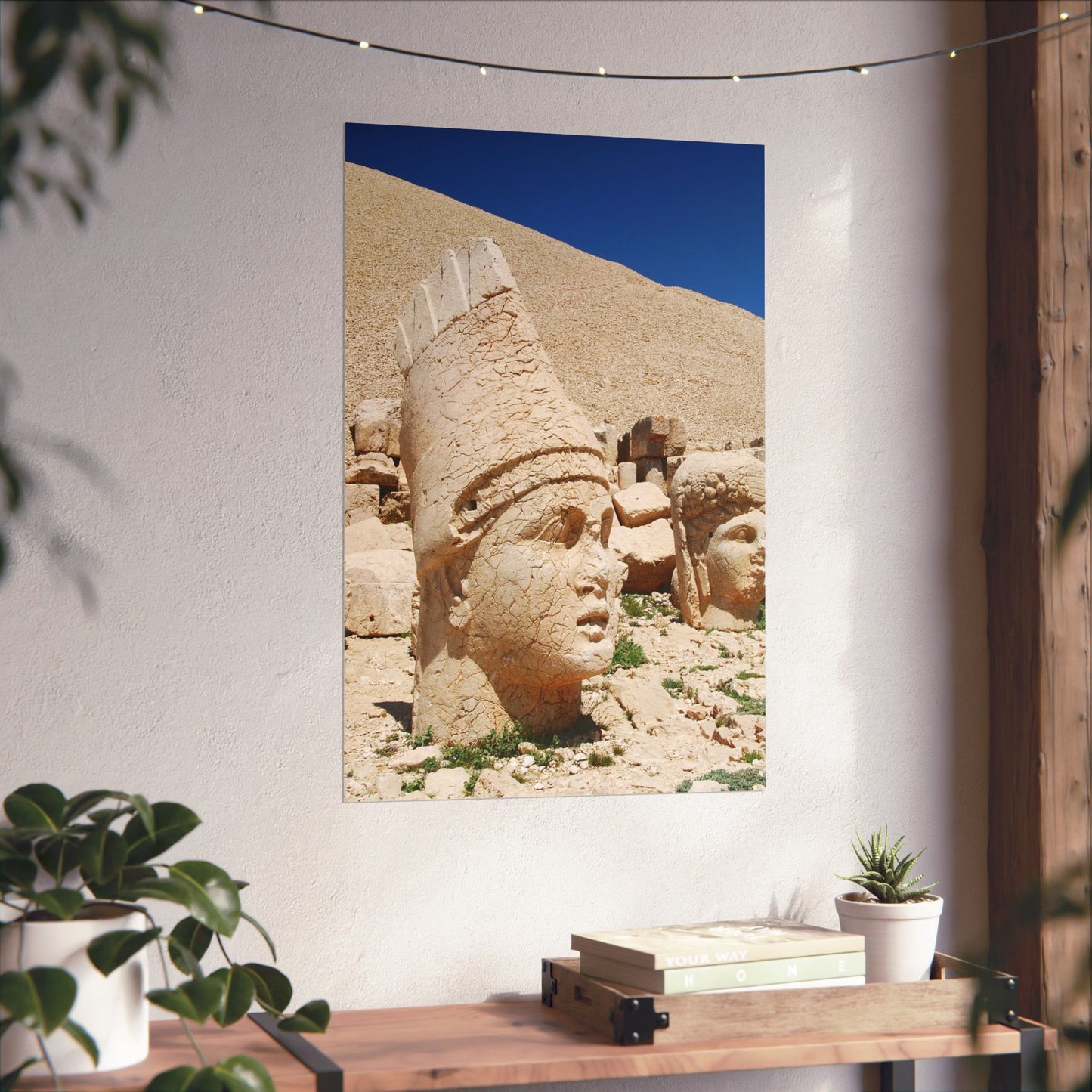 Wall art of ancient stone carvings on a white wall with plants and books below.