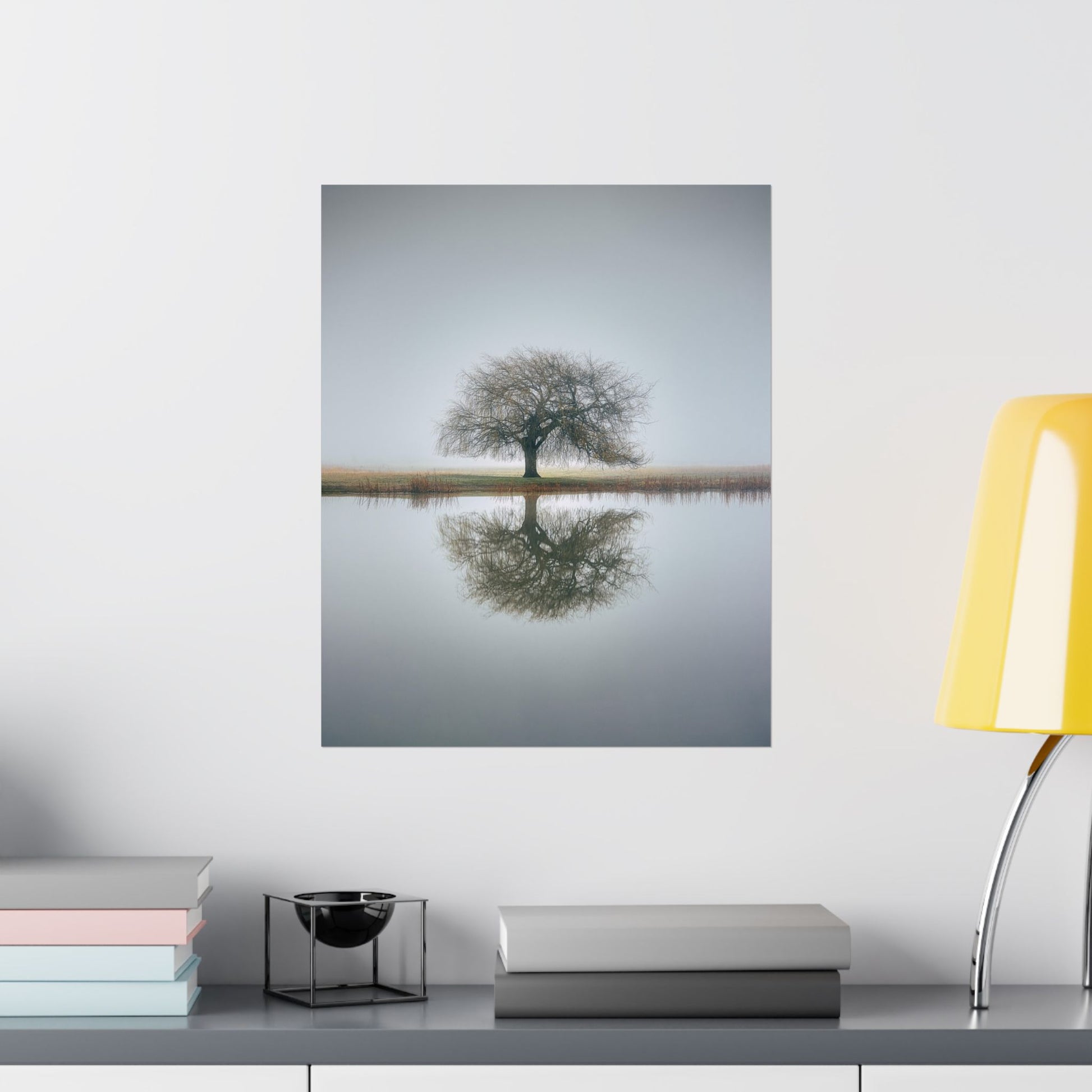 Framed artwork of a tree reflected in water on a wall above a shelf with books and decor items.
