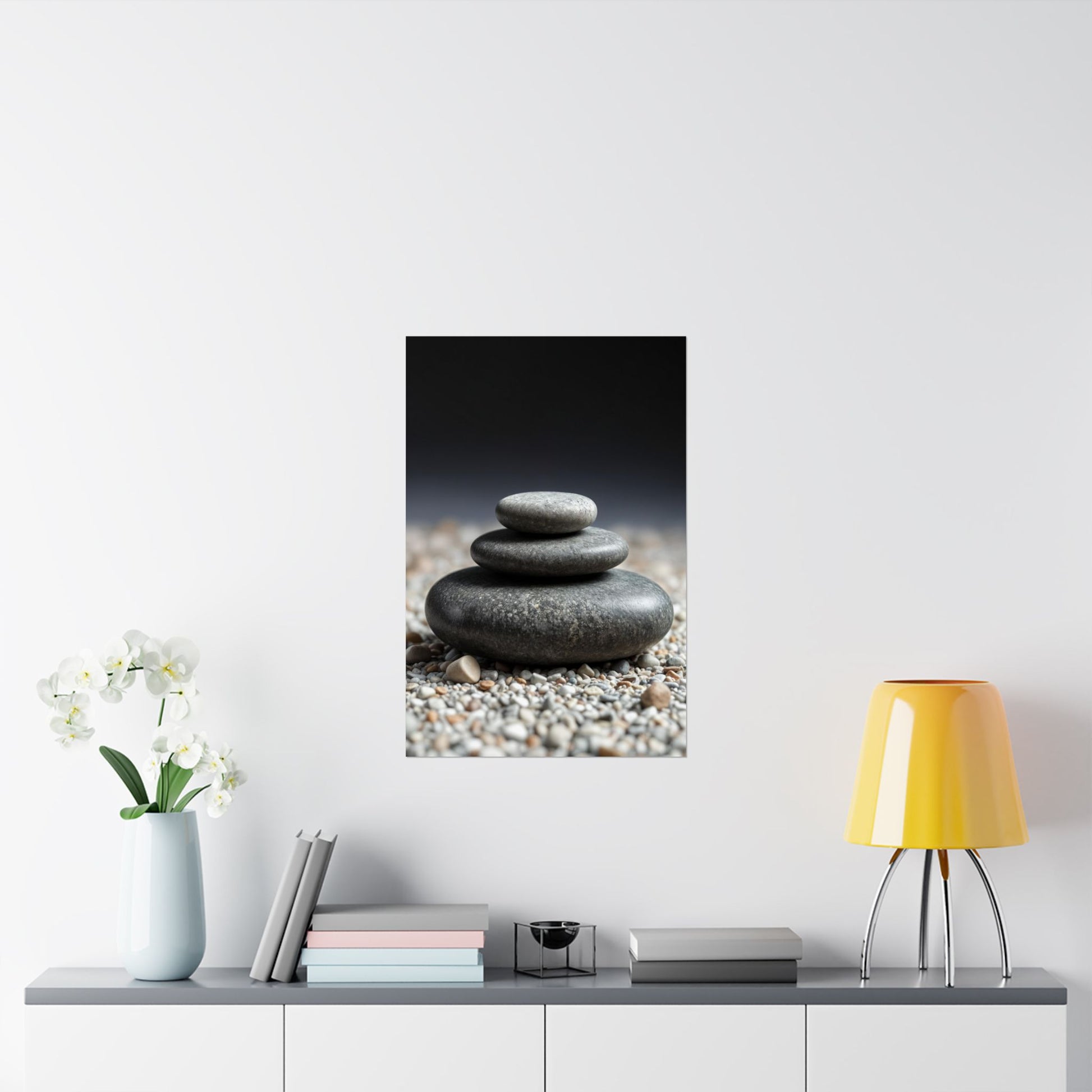 Framed artwork of stacked stones on a wall above a table with decor items.