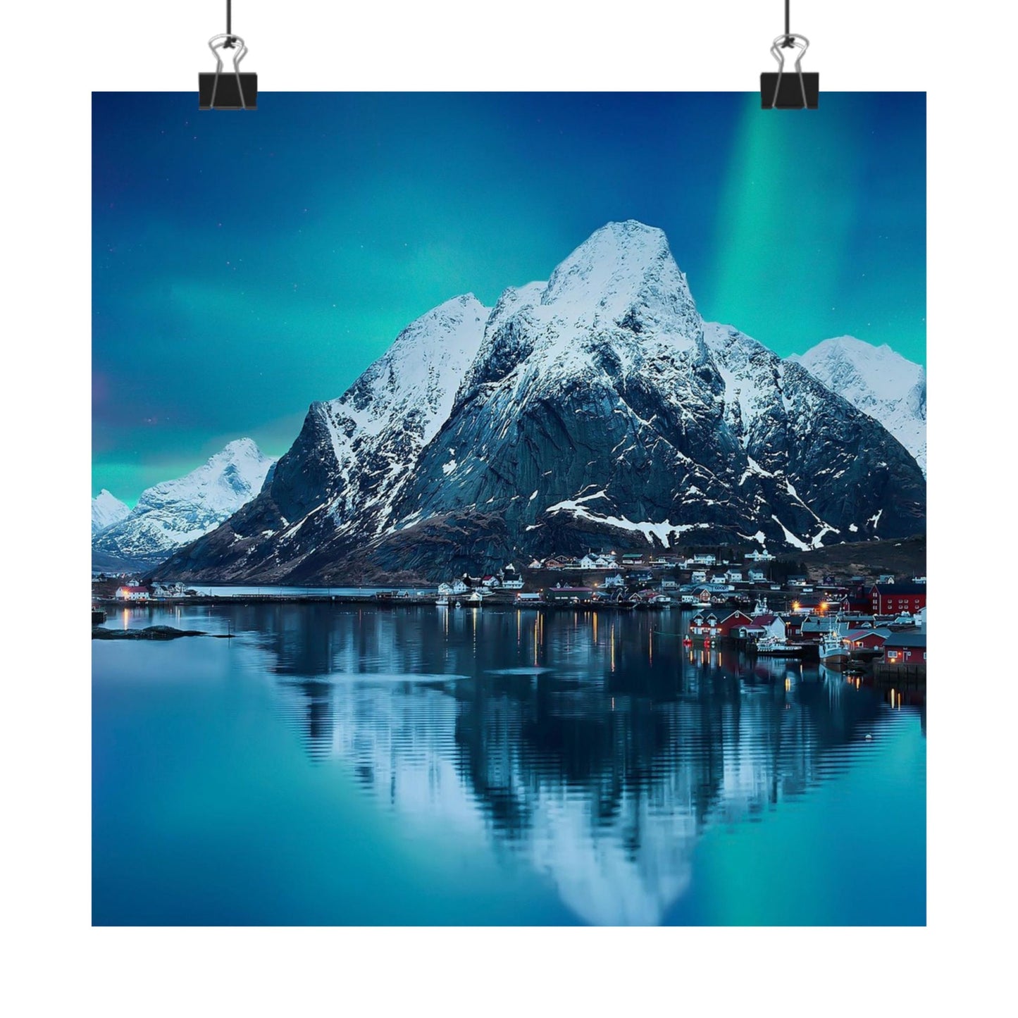 Snow-covered mountain reflecting in a lake with a town below under a dark blue sky.