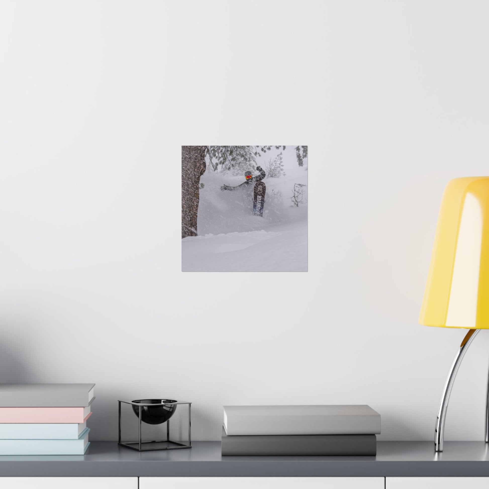 Framed photograph of a person in a snowy landscape on a wall above a desk with books and a lamp.