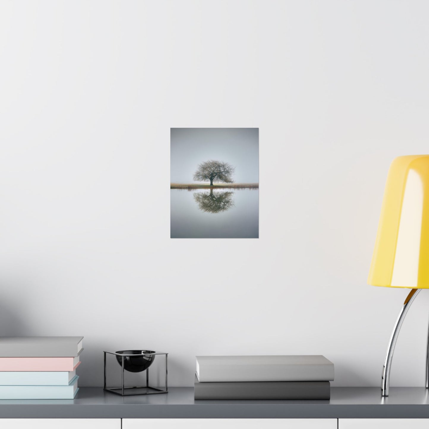 Framed artwork of a tree on a white wall above a desk with books and a lamp.