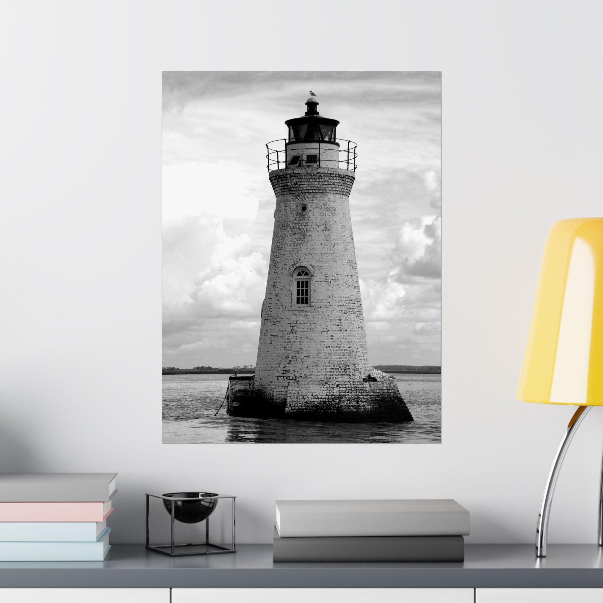 Poster of a lighthouse on a wall above a shelf with books and decor items.