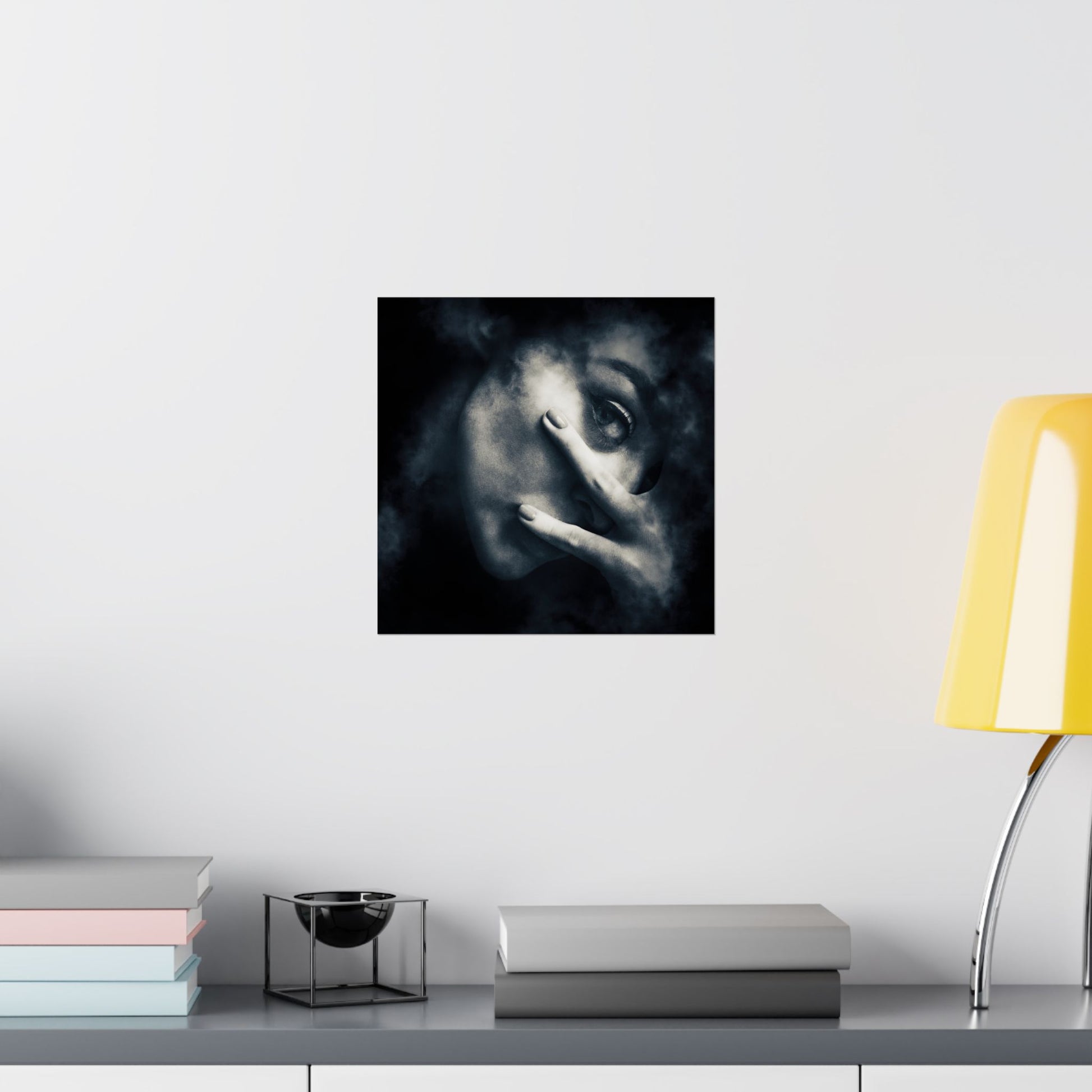 Framed artwork of a stylized face on a wall above a shelf with books and a lamp.