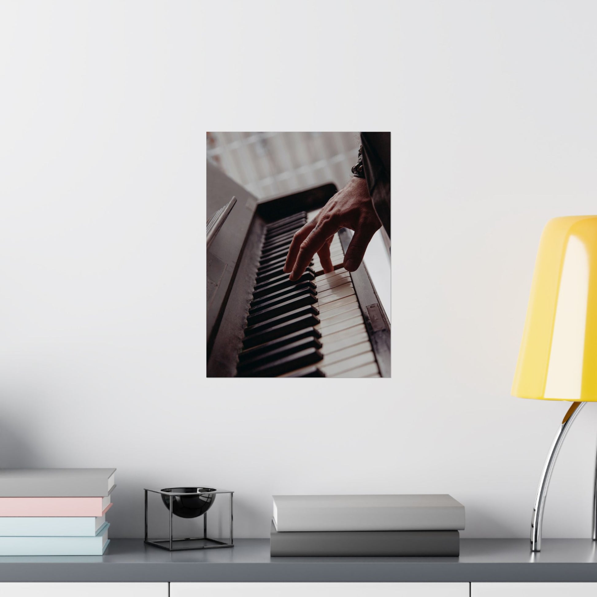 Framed picture of hands playing a piano on a shelf with books and a lamp.