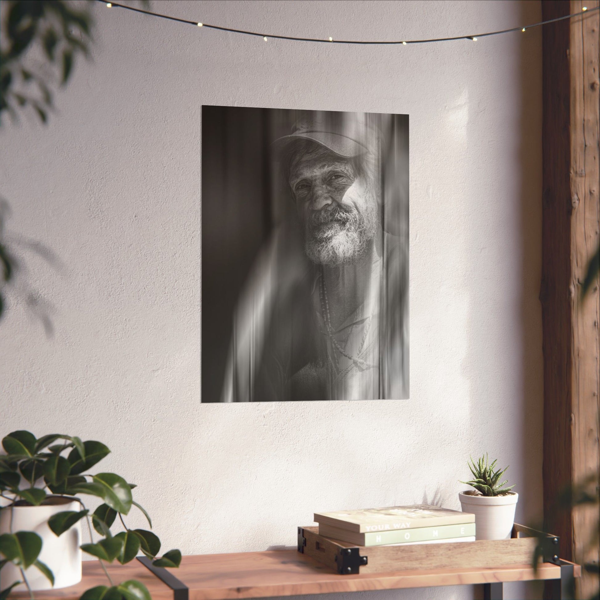 Black and white portrait of a man with a beard hanging on a wall above a wooden shelf with books and plants.