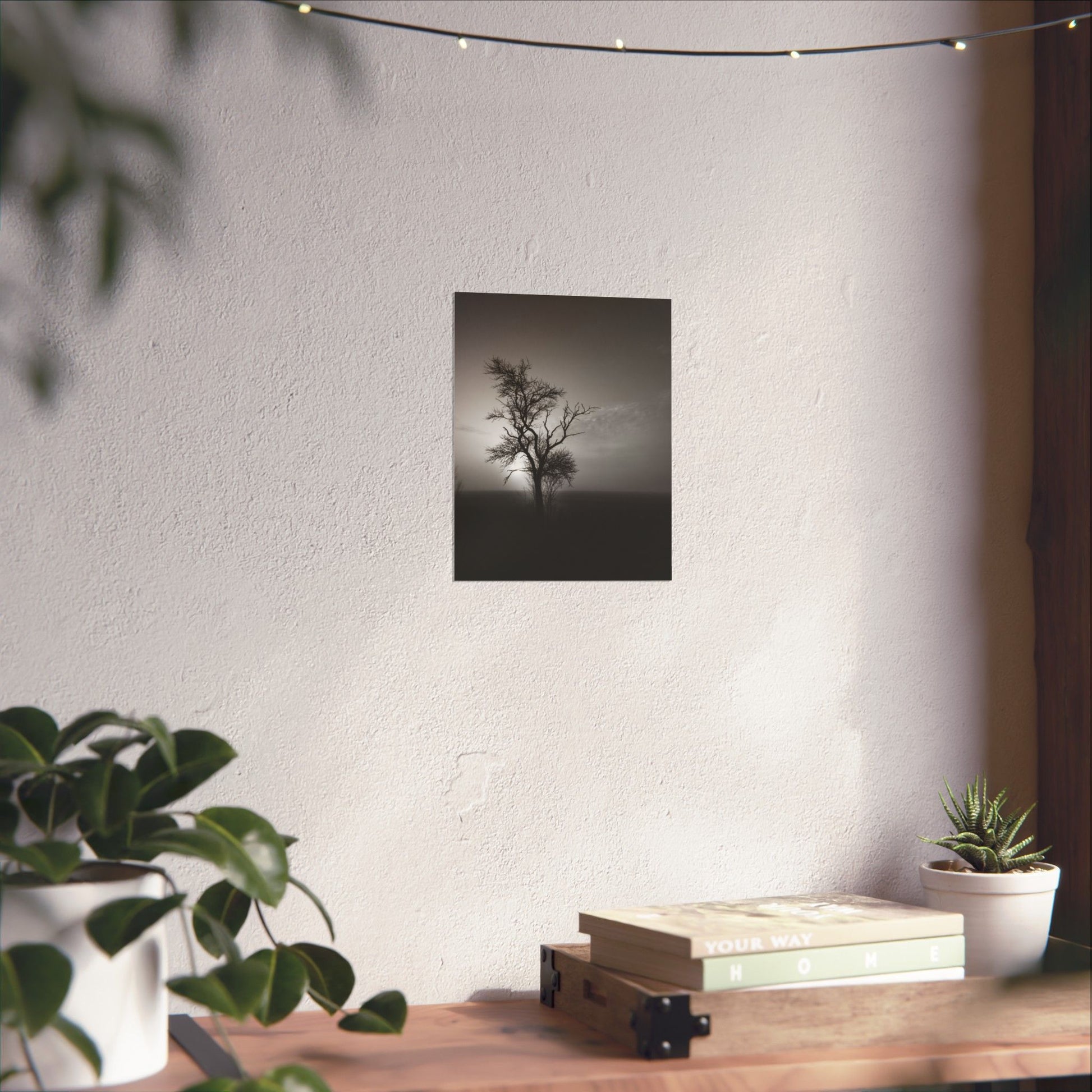 Art print of a tree on a wall above a wooden table with plants and books.