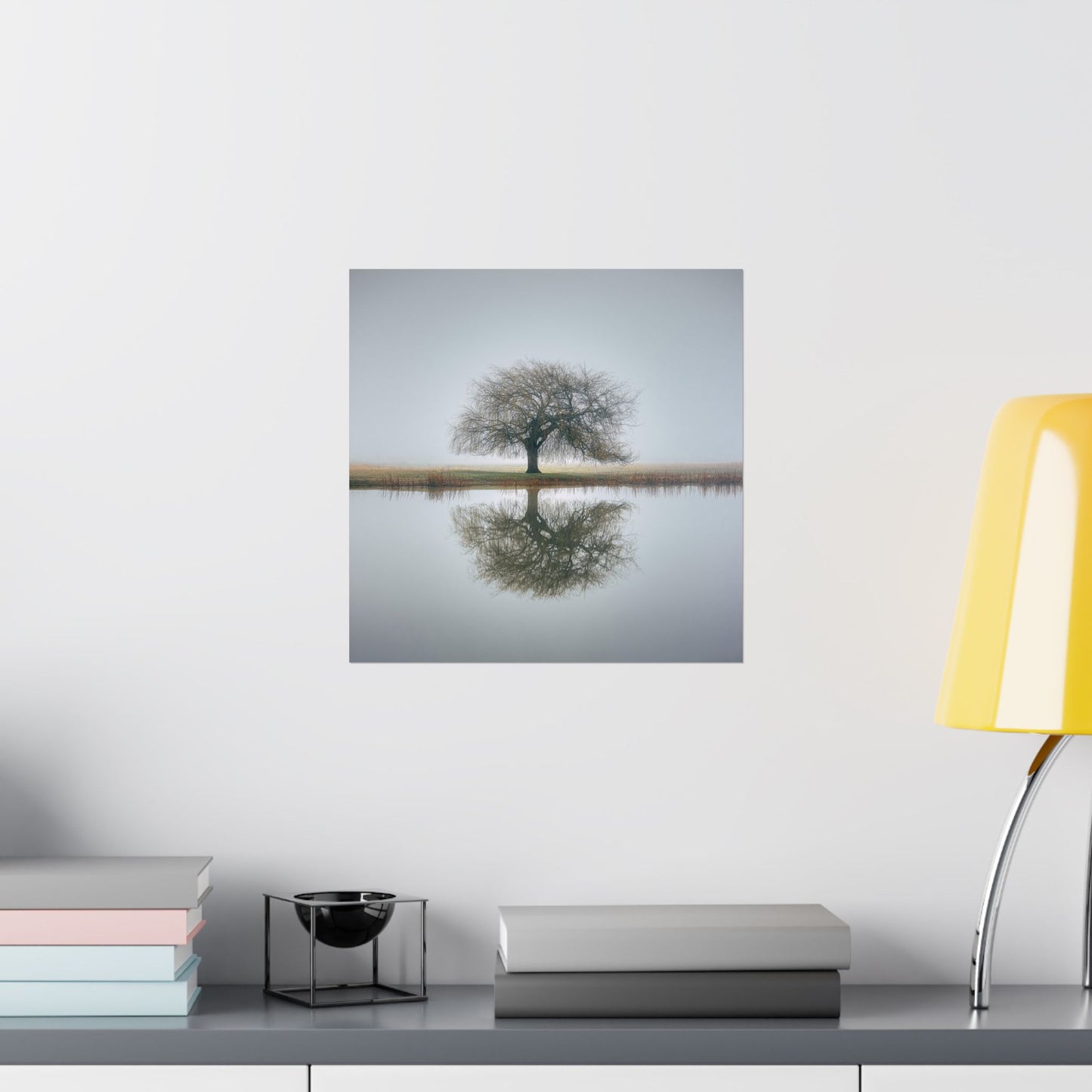 Wall art of a tree reflected in water on a white wall above a shelf.