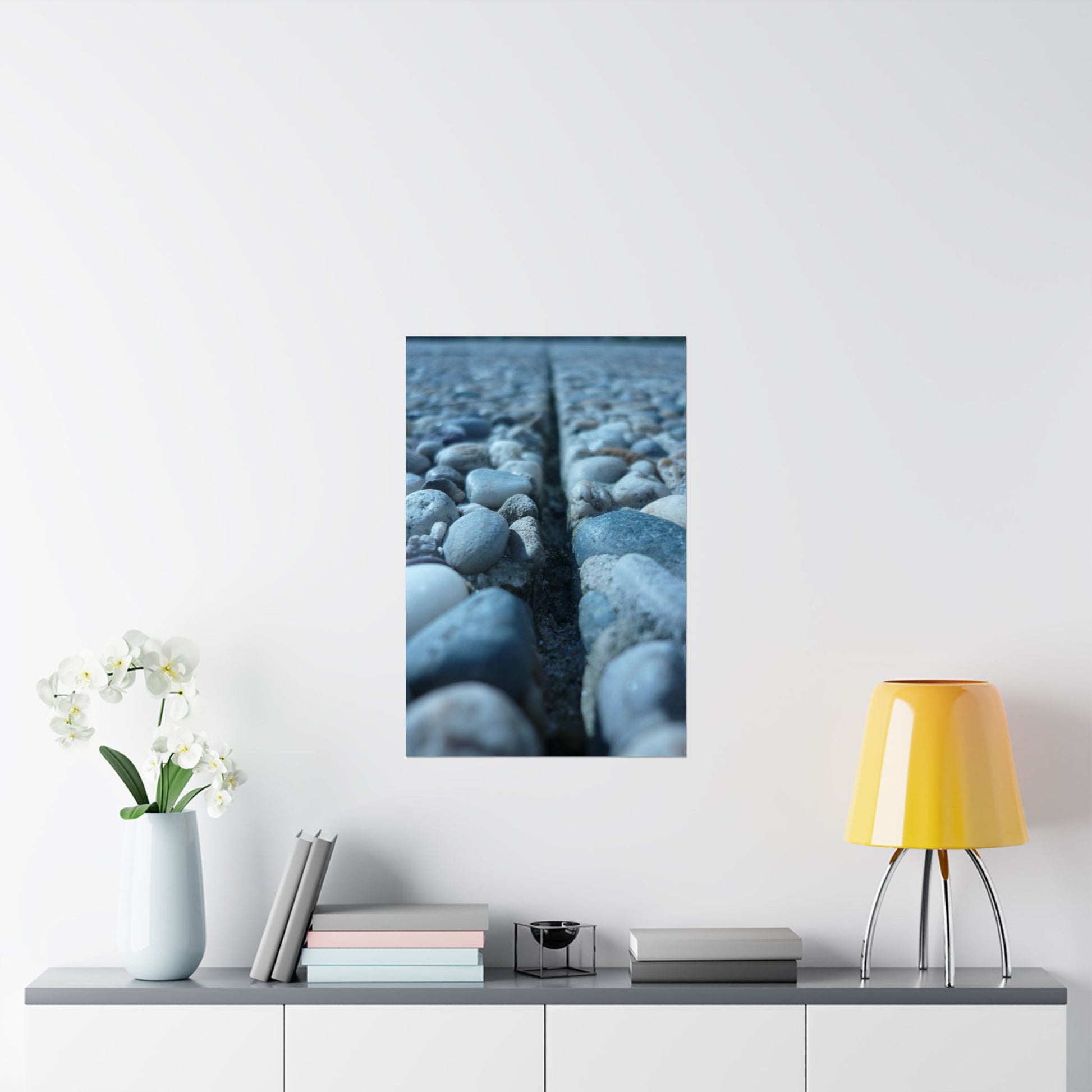 Framed artwork of pebbles on a white wall above a shelf with decor items.