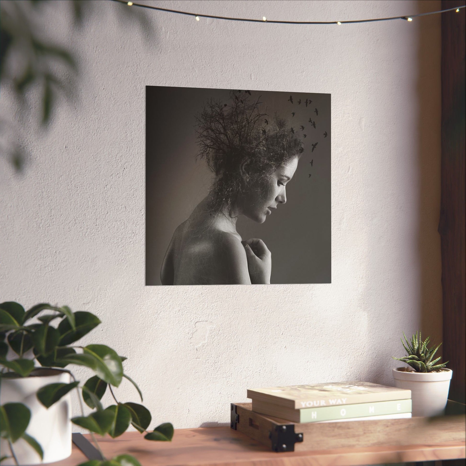 Framed black and white portrait of a woman with birds on a wall above a wooden desk with plants.