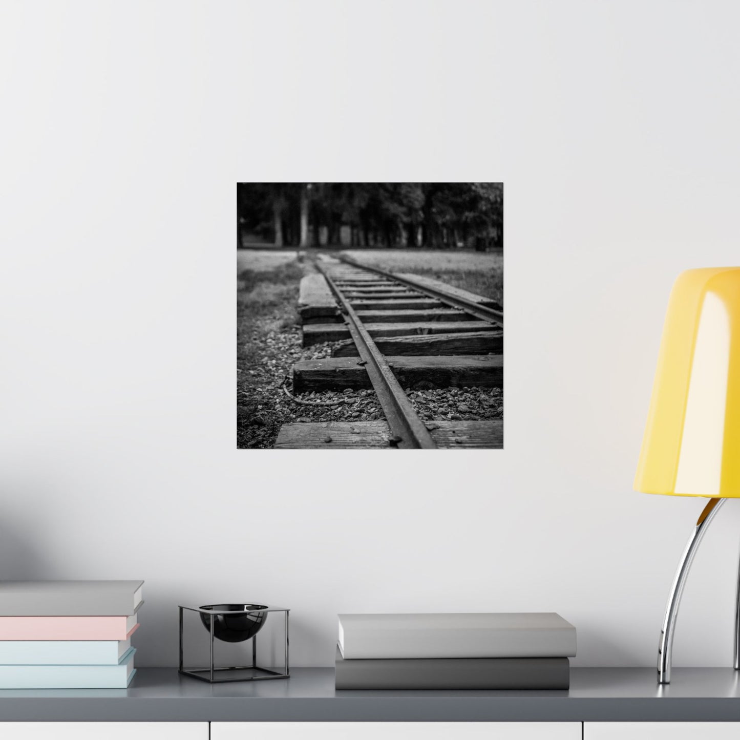 Black and white photograph of a railway track on a wall above a shelf with books and decor.