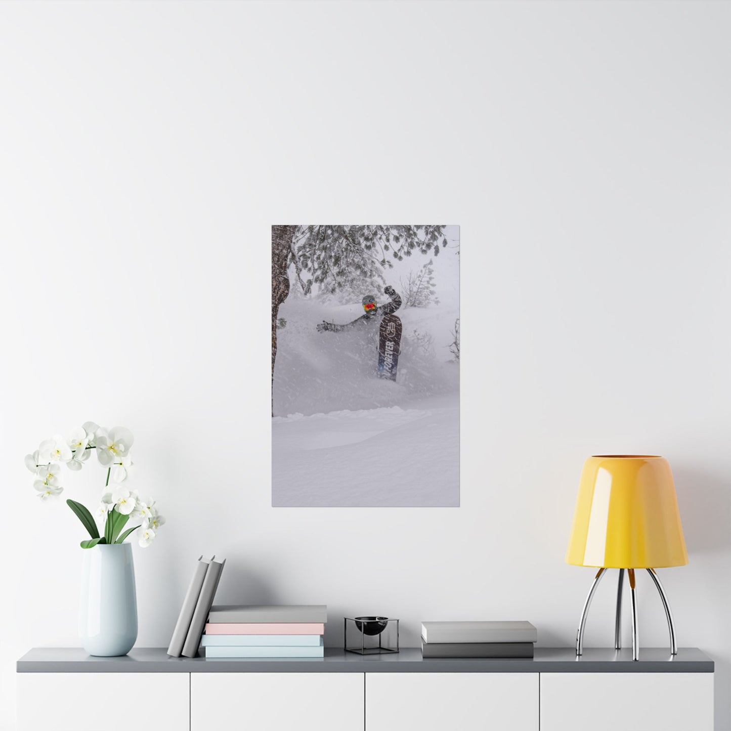 Framed photograph of a person in a snowy landscape hanging on a white wall above a shelf with decor items.