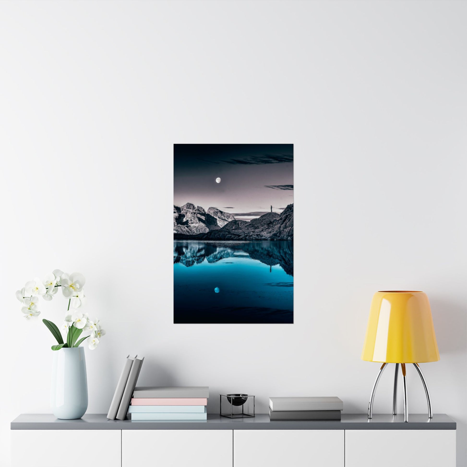 Framed mountain landscape print on a wall above a shelf with decor items.