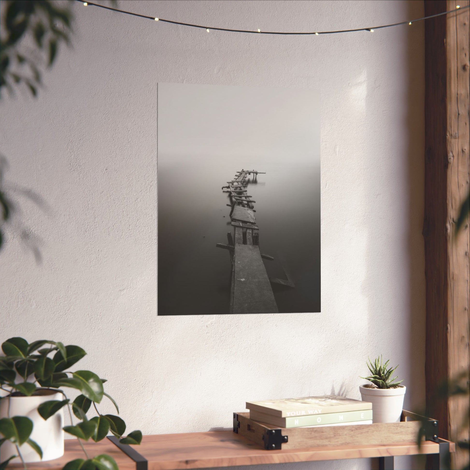 Black and white abstract art piece on a white wall with plants and books below.
