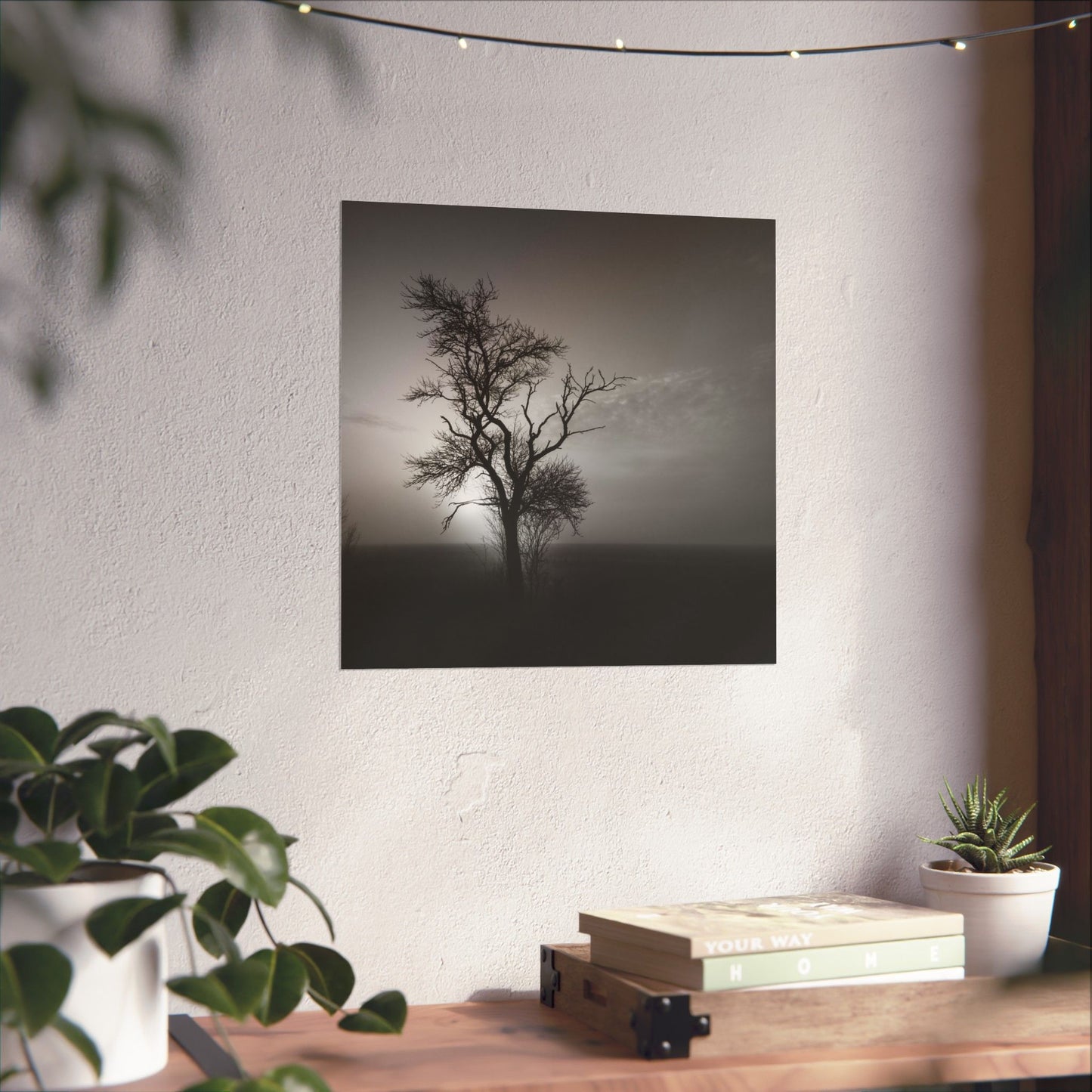 Framed black and white tree print on a wall above a wooden desk with plants.