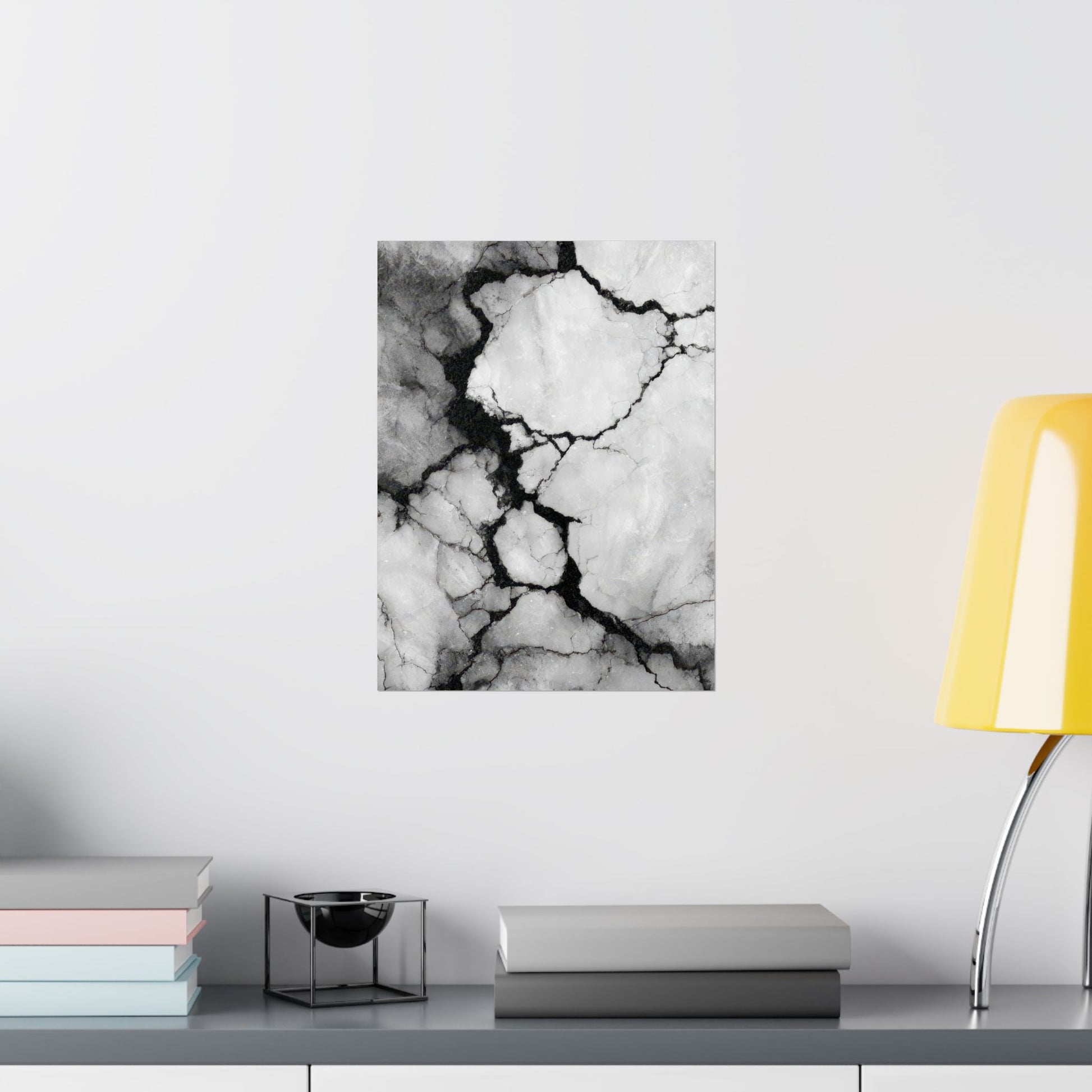 Black and white marble patterned wall art on a white wall with books and a lamp in the foreground.