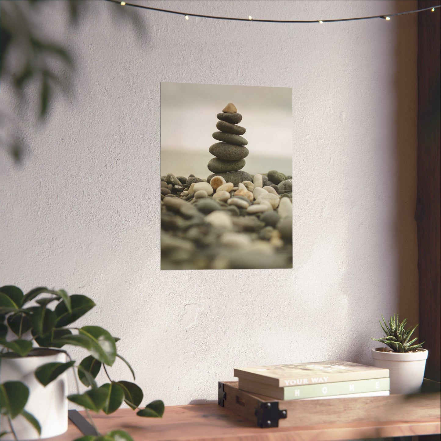 Stylized photo of stacked stones on a wall with plants and books on a table below.