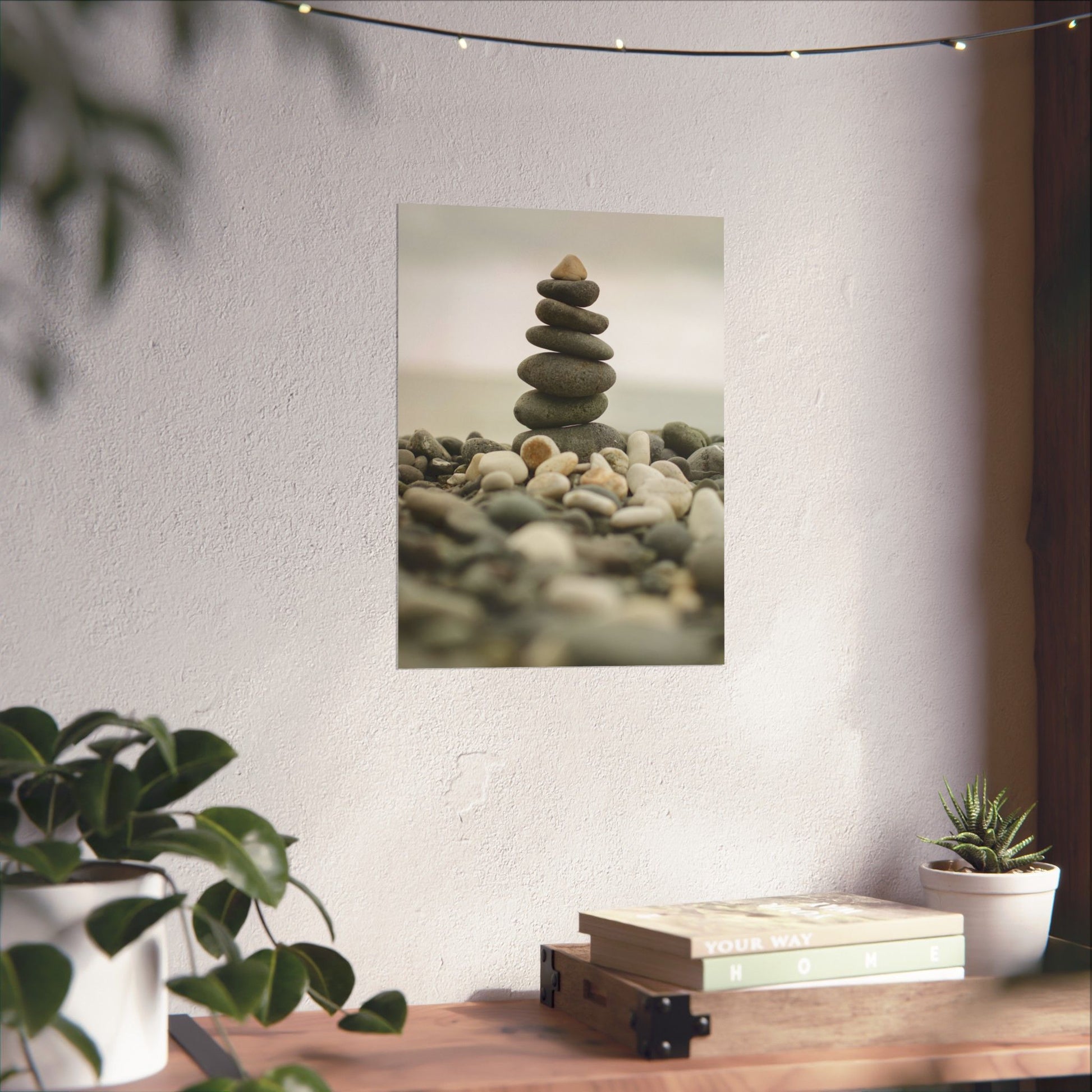 Stylized photo of stacked stones on a wall with plants and books on a table below.
