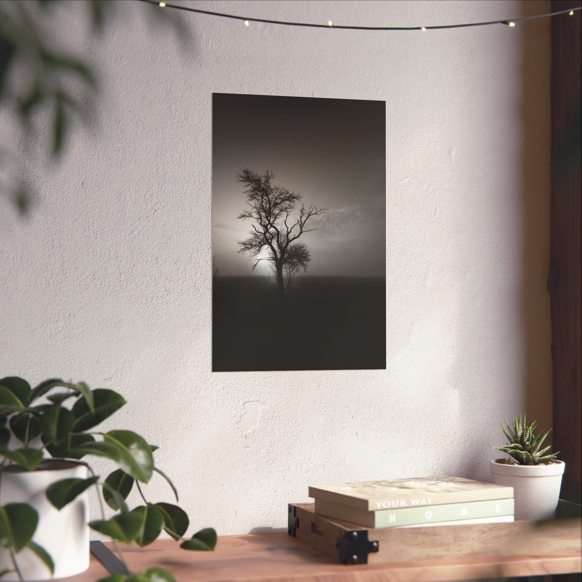 Framed black and white tree print on a wall above a wooden desk with plants.