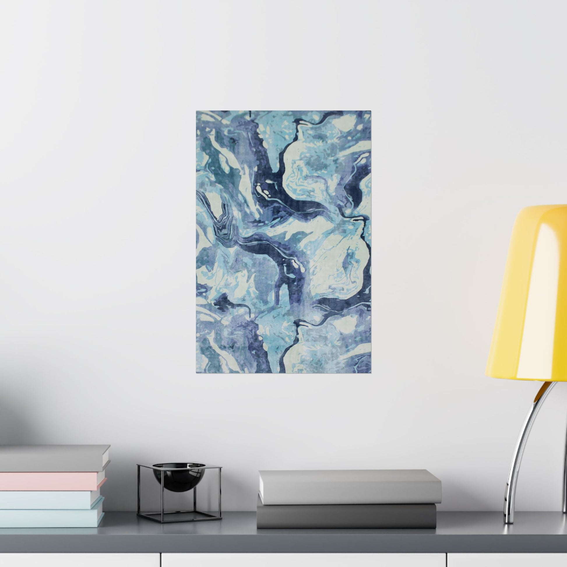 Abstract blue and white painting on a wall above a shelf with books and a lamp.