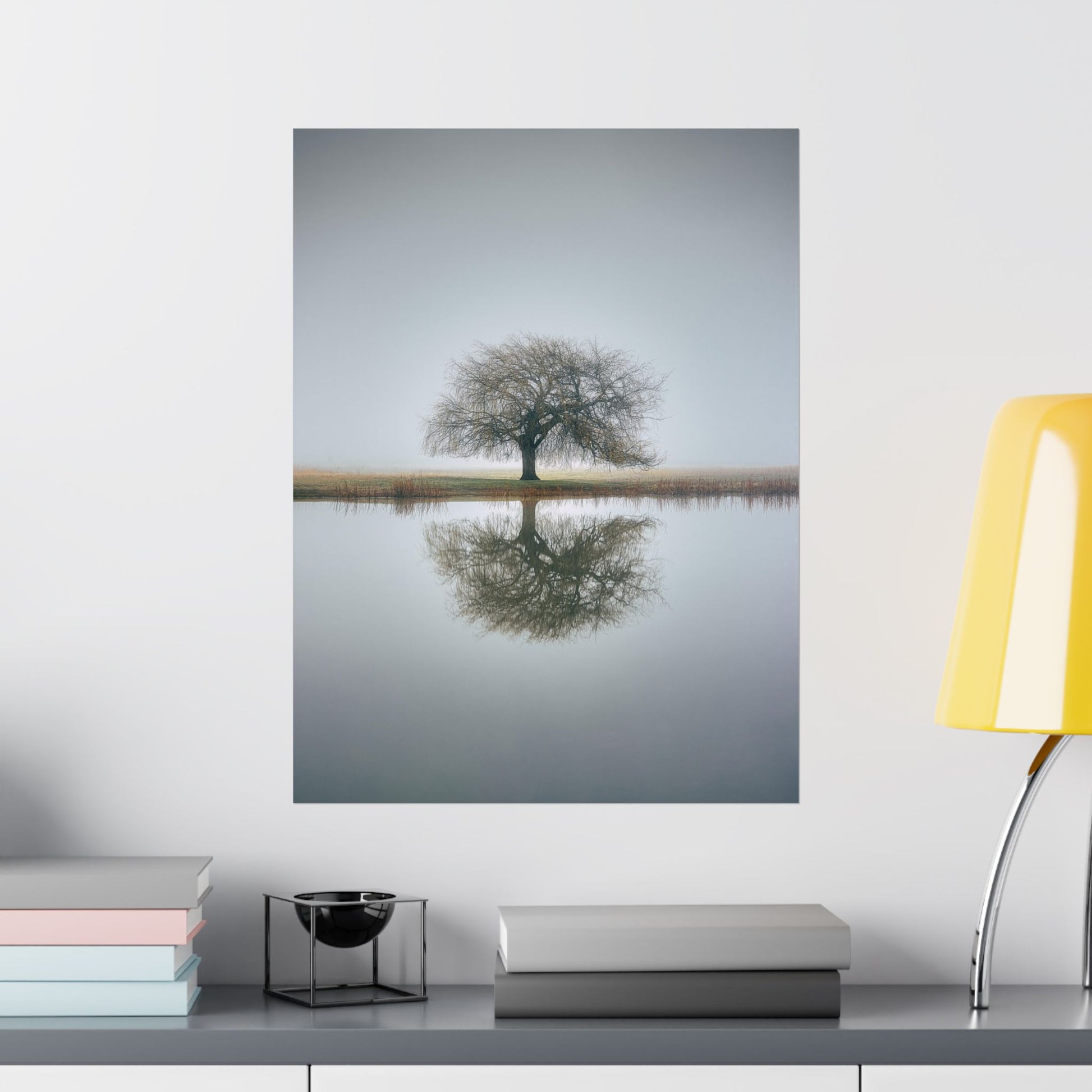 Framed photograph of a tree reflected in water on a wall above a shelf with books and decor items.