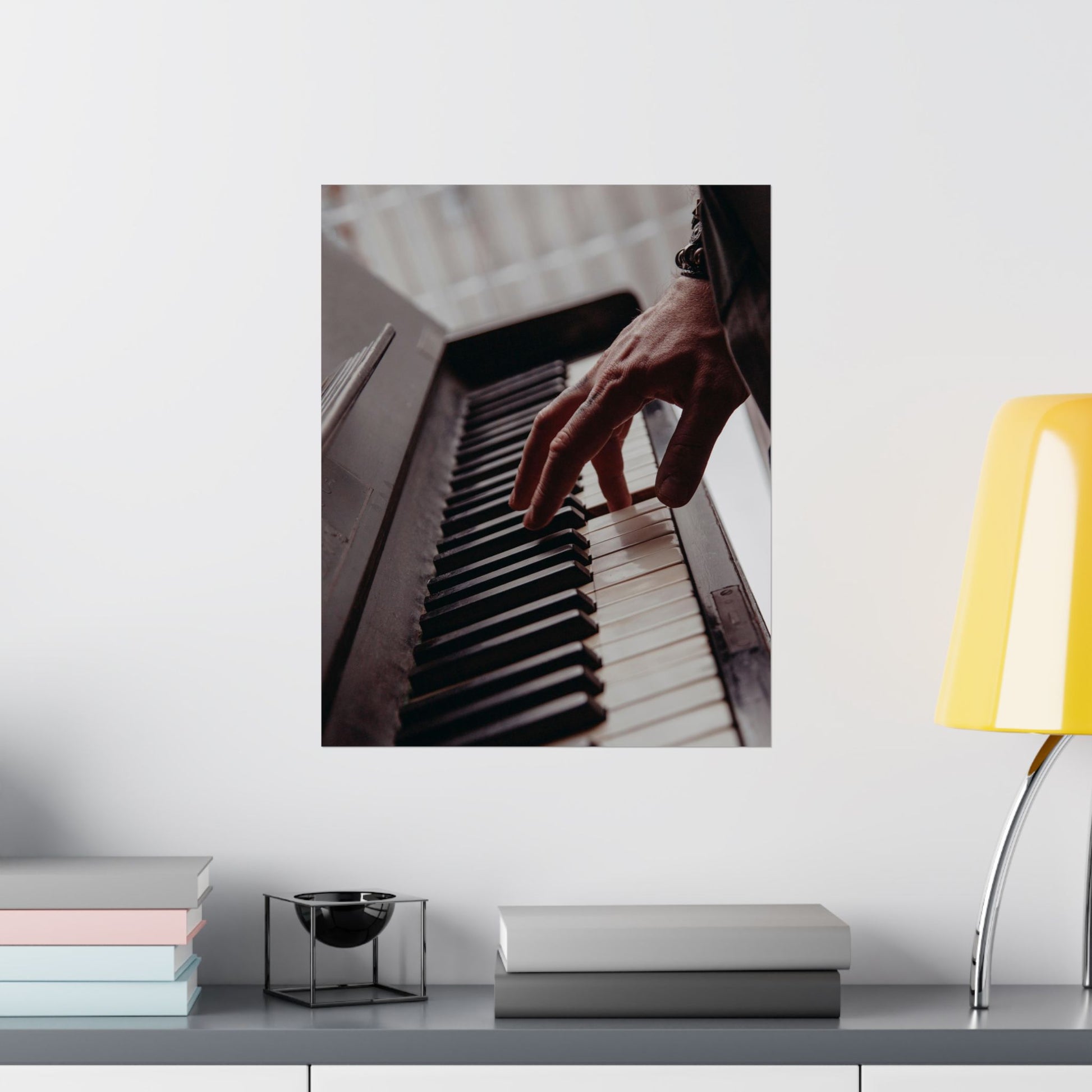 Framed artwork of a hand playing piano on a wall above a desk with books and a lamp.