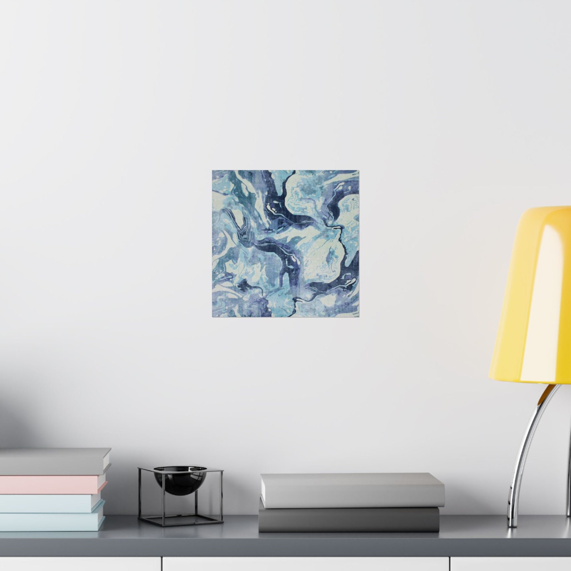 Abstract blue and white painting on a wall above a shelf with books and a lamp.