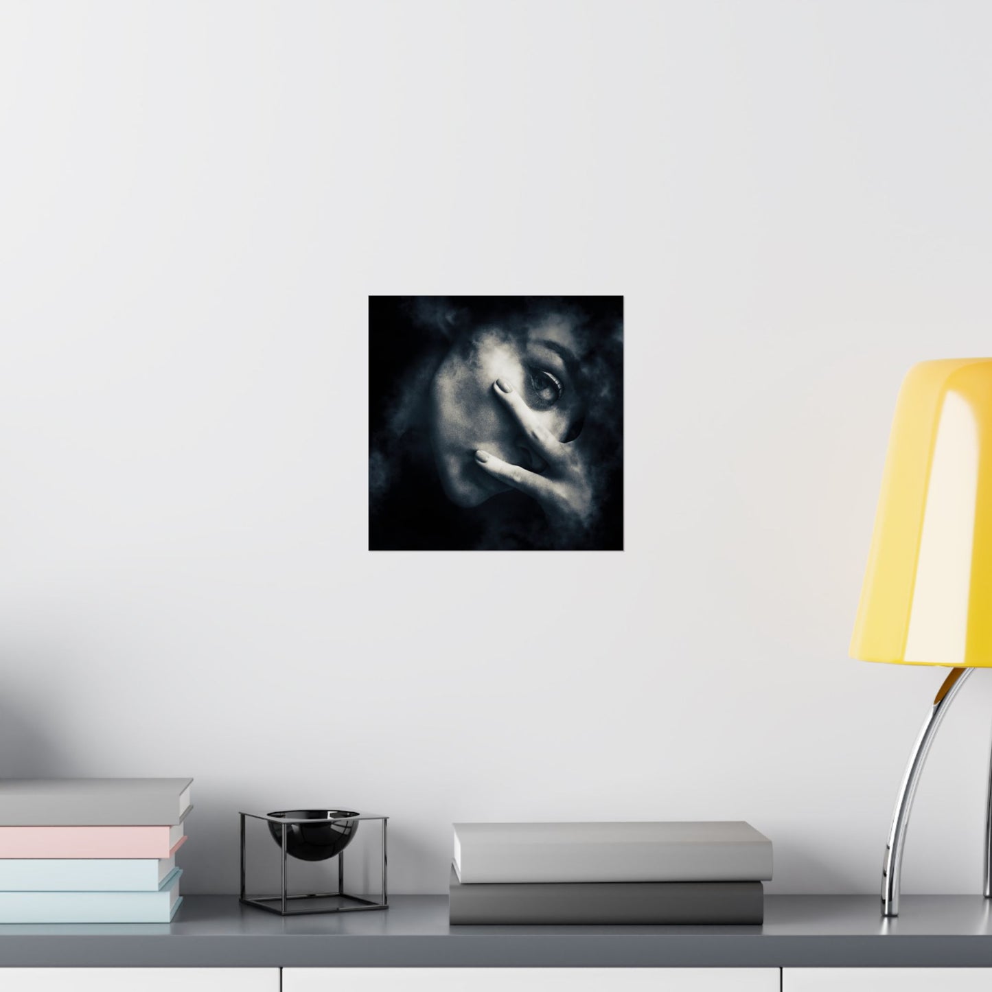 Framed artwork of a stylized face on a wall above a desk with books and a lamp.