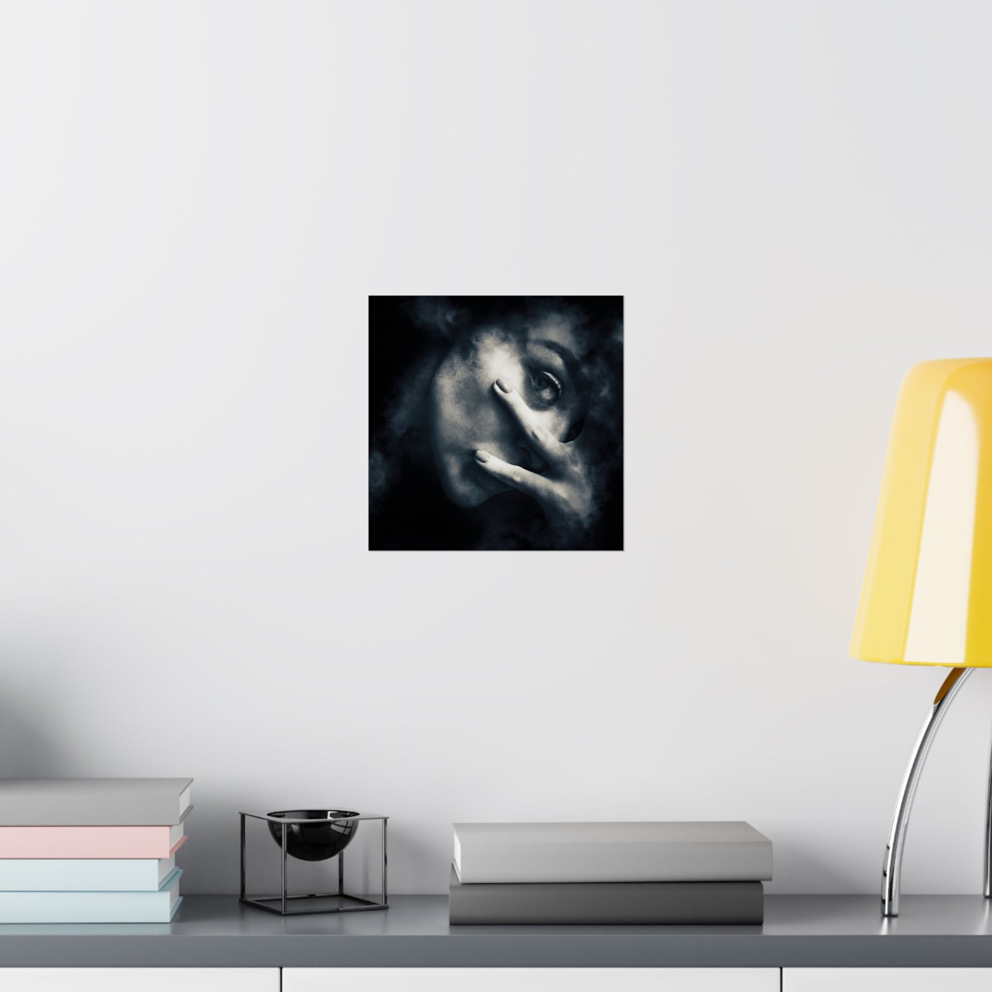 Framed artwork of a stylized face on a wall above a desk with books and a lamp.