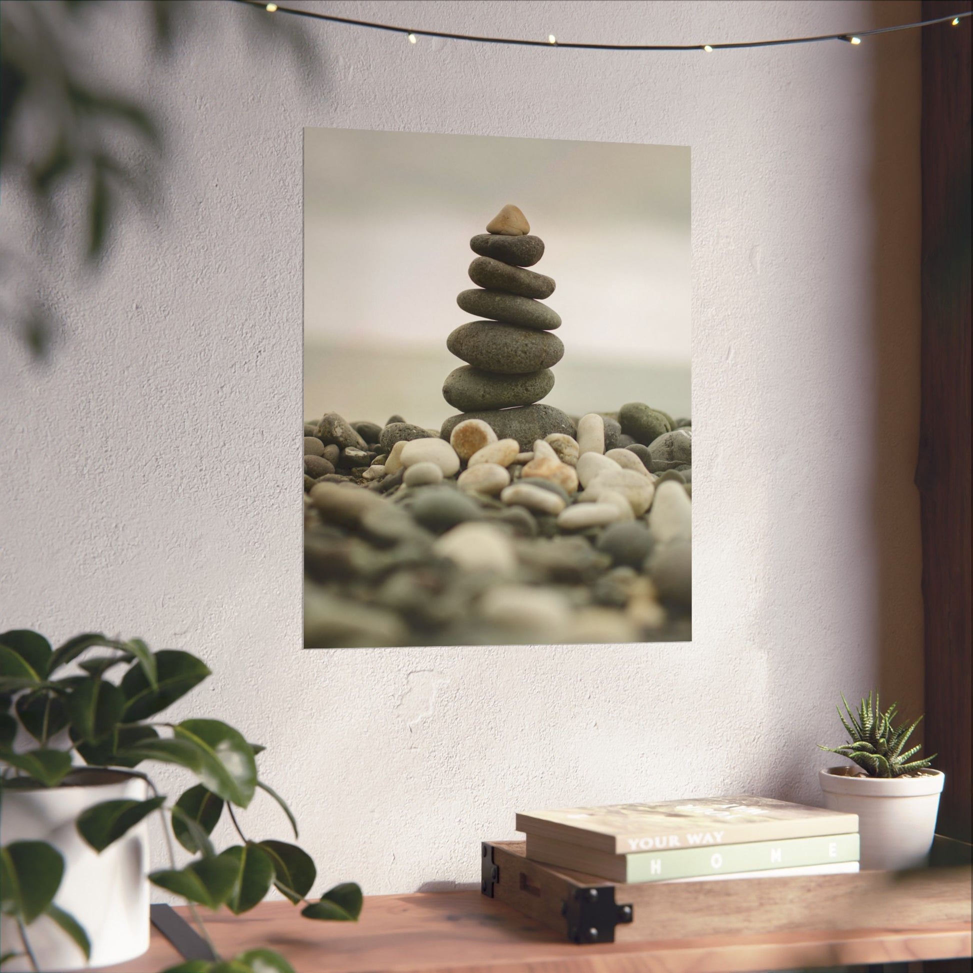 Stylized photo of stacked stones on a wall with plants and books on a table below.