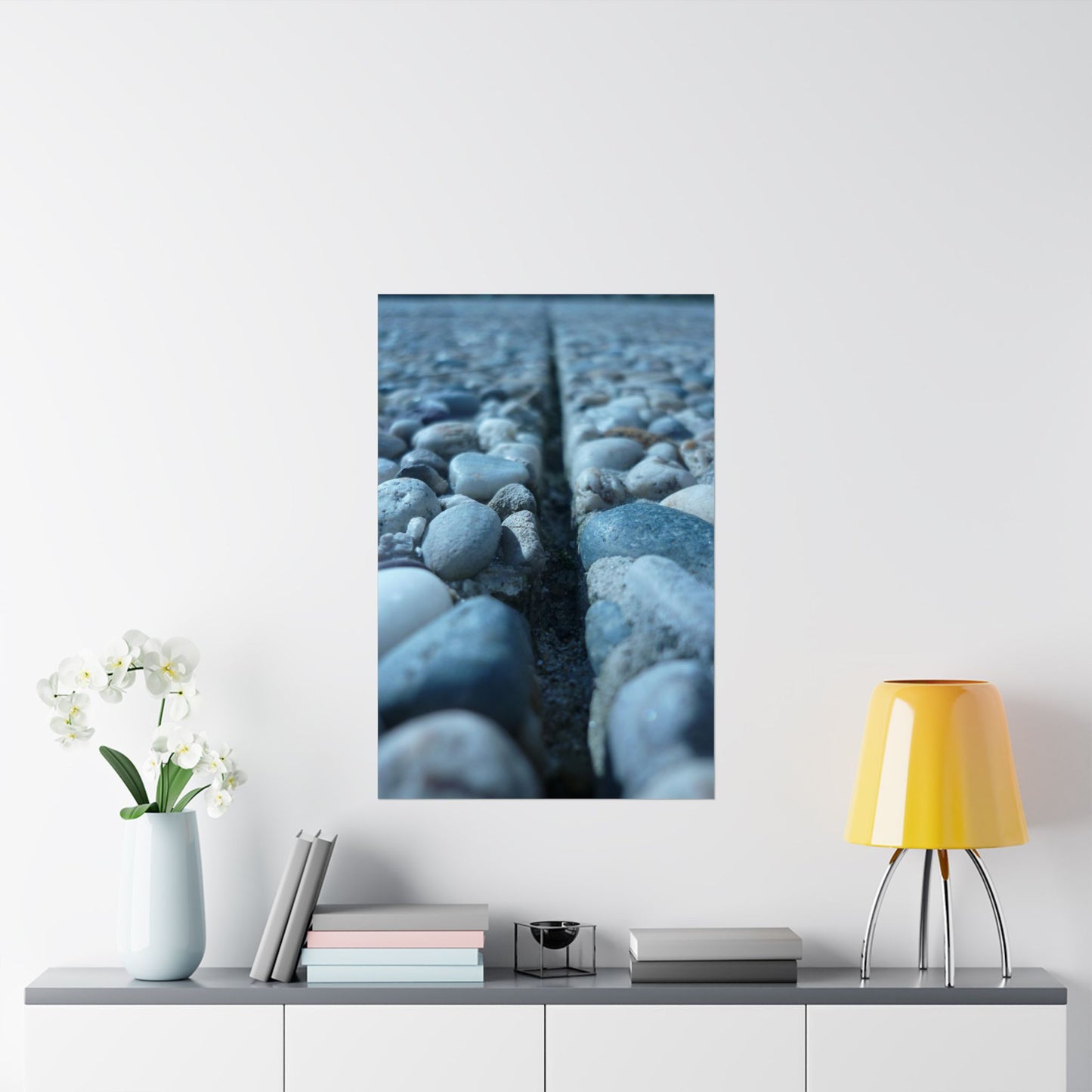 Framed artwork of pebbles on a white wall above a shelf with decor items.