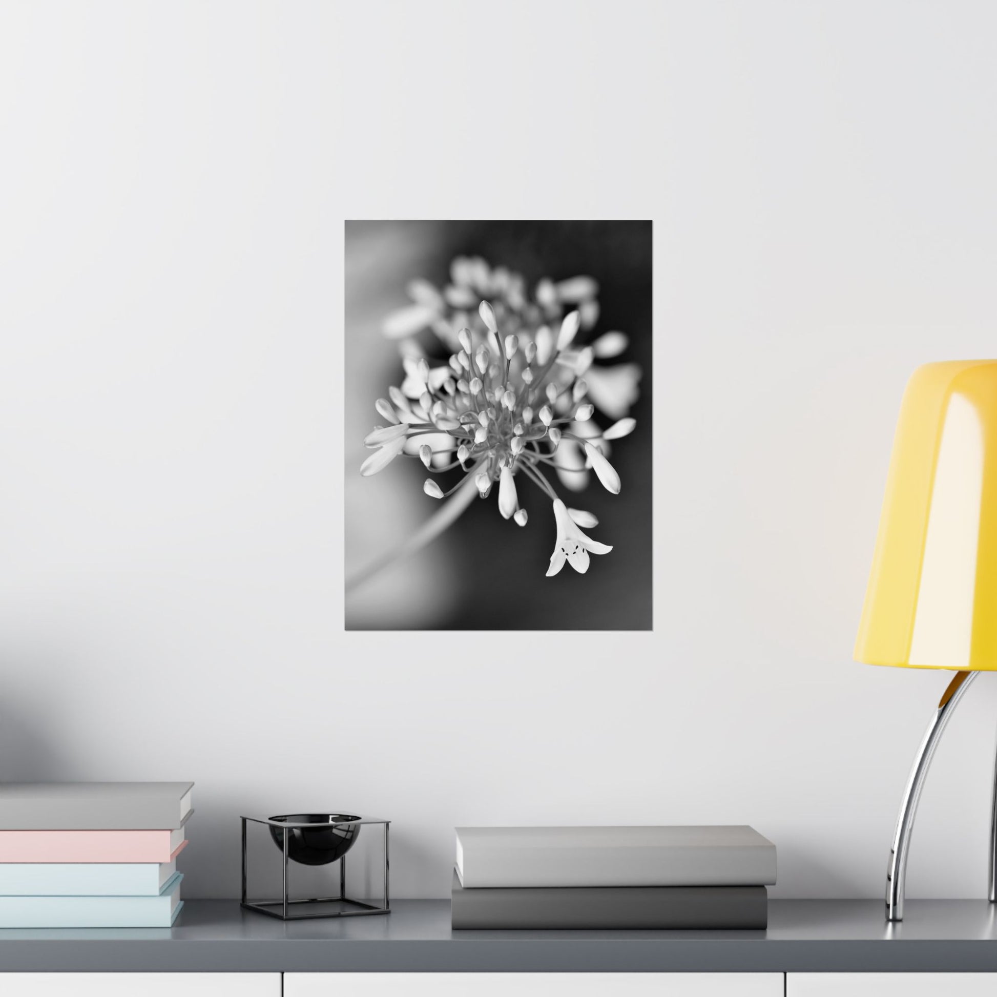 Framed black and white floral print on a wall above a desk with books and a lamp.