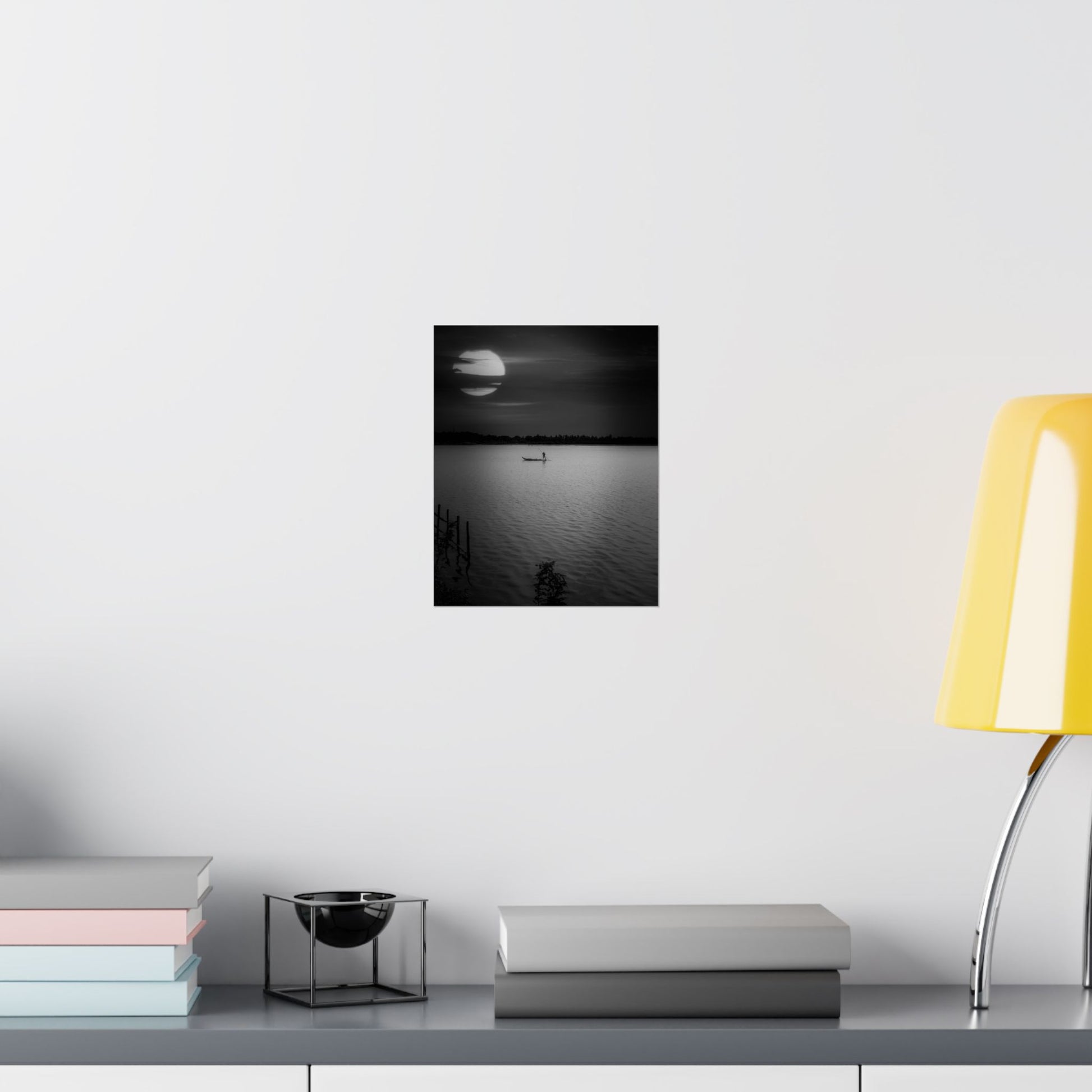 Framed black and white artwork on a wall above a desk with books and a lamp.