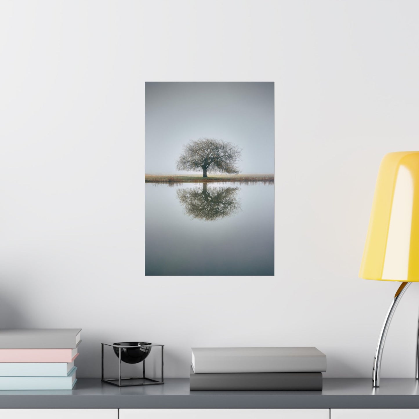 Framed artwork of a tree reflected in water on a wall above a desk with books and a lamp.