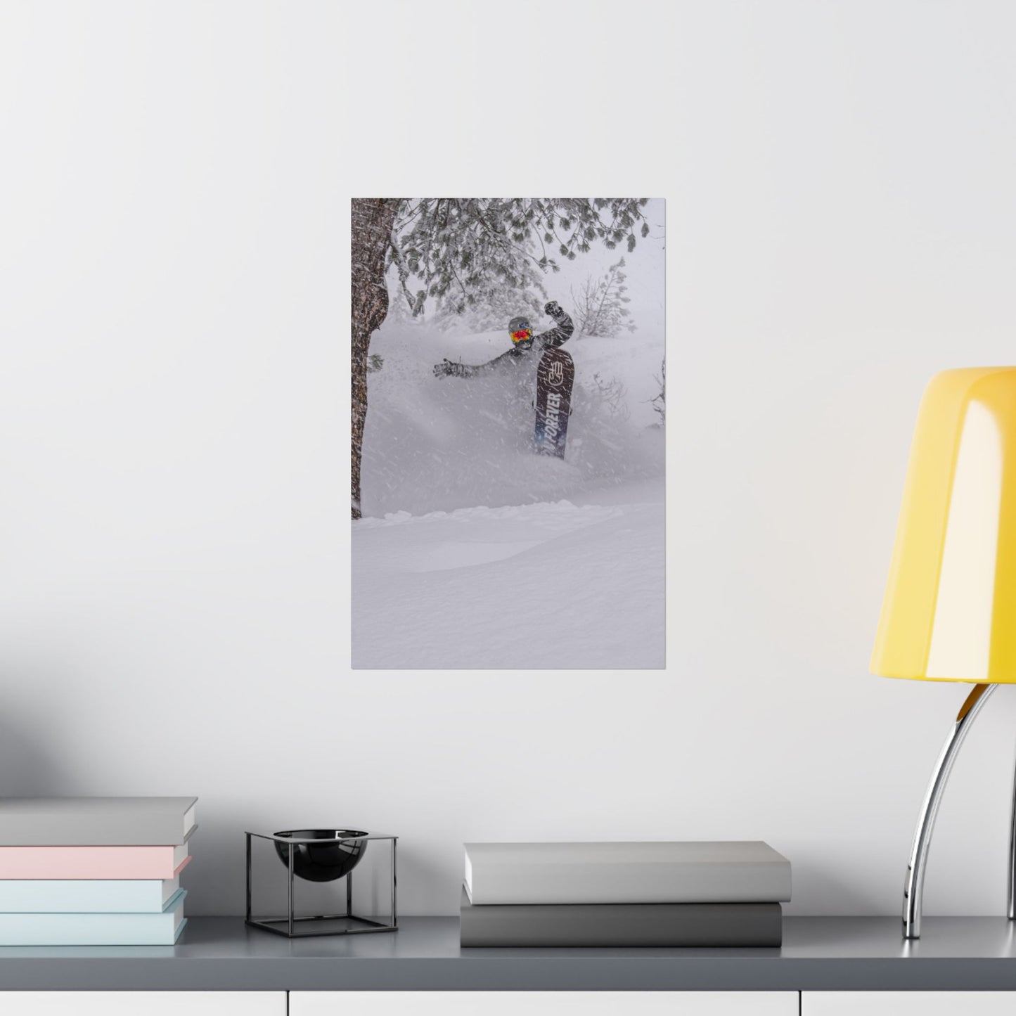 Poster of a person in a snowy landscape on a wall above a desk with books and a lamp.