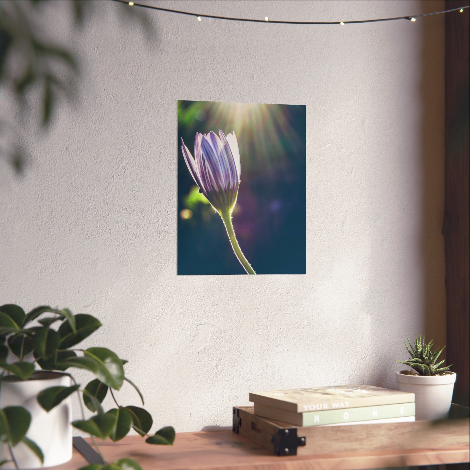 Flower poster on a wall with plants and books on a table below.