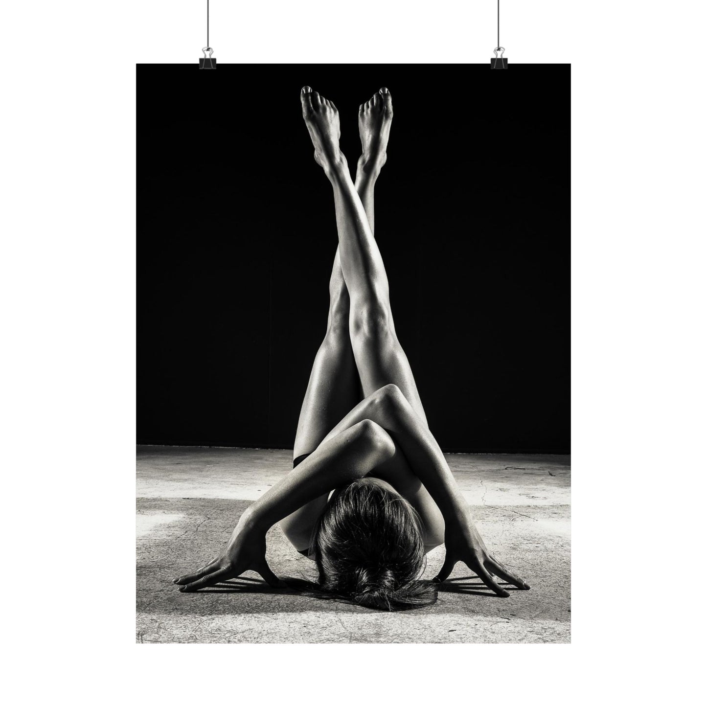 Black and white photo of a person in a yoga pose with feet in the air against a dark background.
