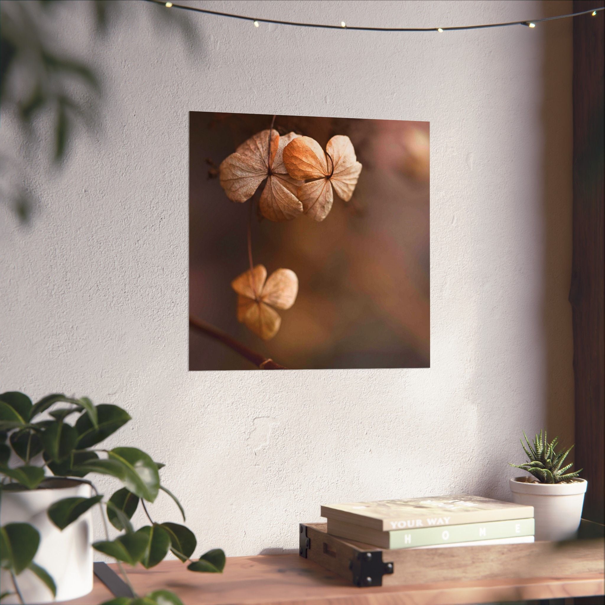 Wall art of dried flowers on a white wall with plants and books below.