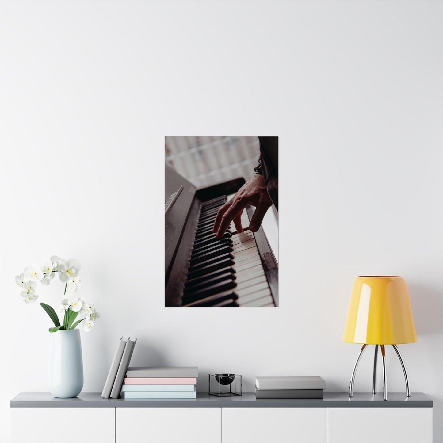 Framed picture of a hand playing piano on a wall above a shelf with decor items.
