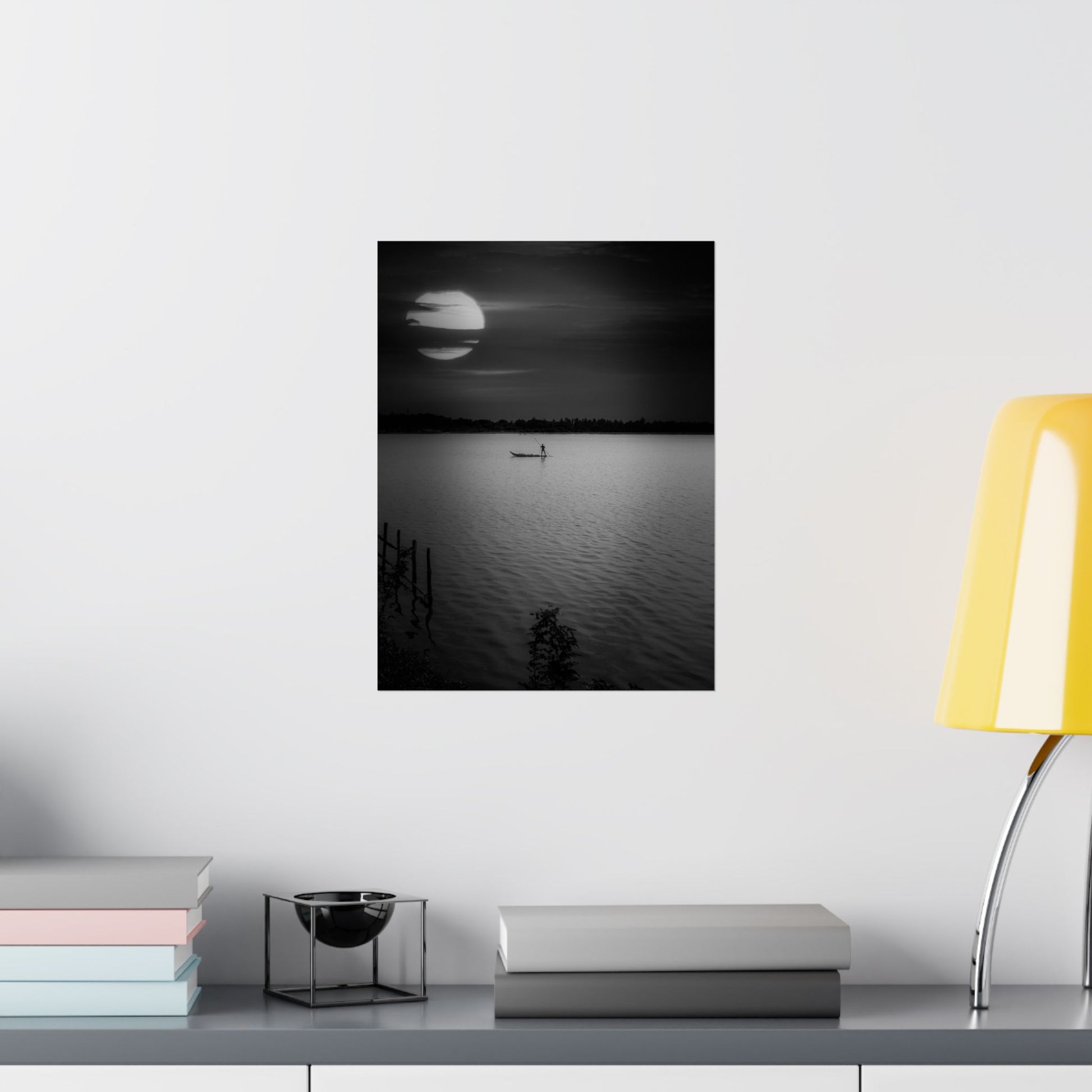 Framed black and white landscape print on a wall above a desk with books and a lamp.