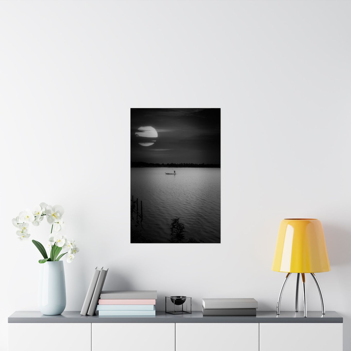 Framed black and white artwork of a moonlit lake on a wall above a shelf with decor items.