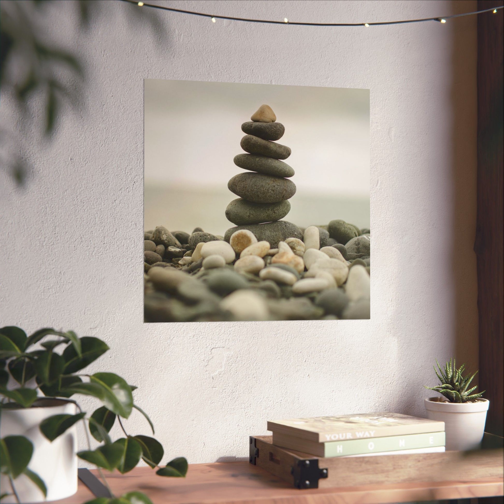 Stack of stones on pebbles with indoor plants and books on a wooden surface.