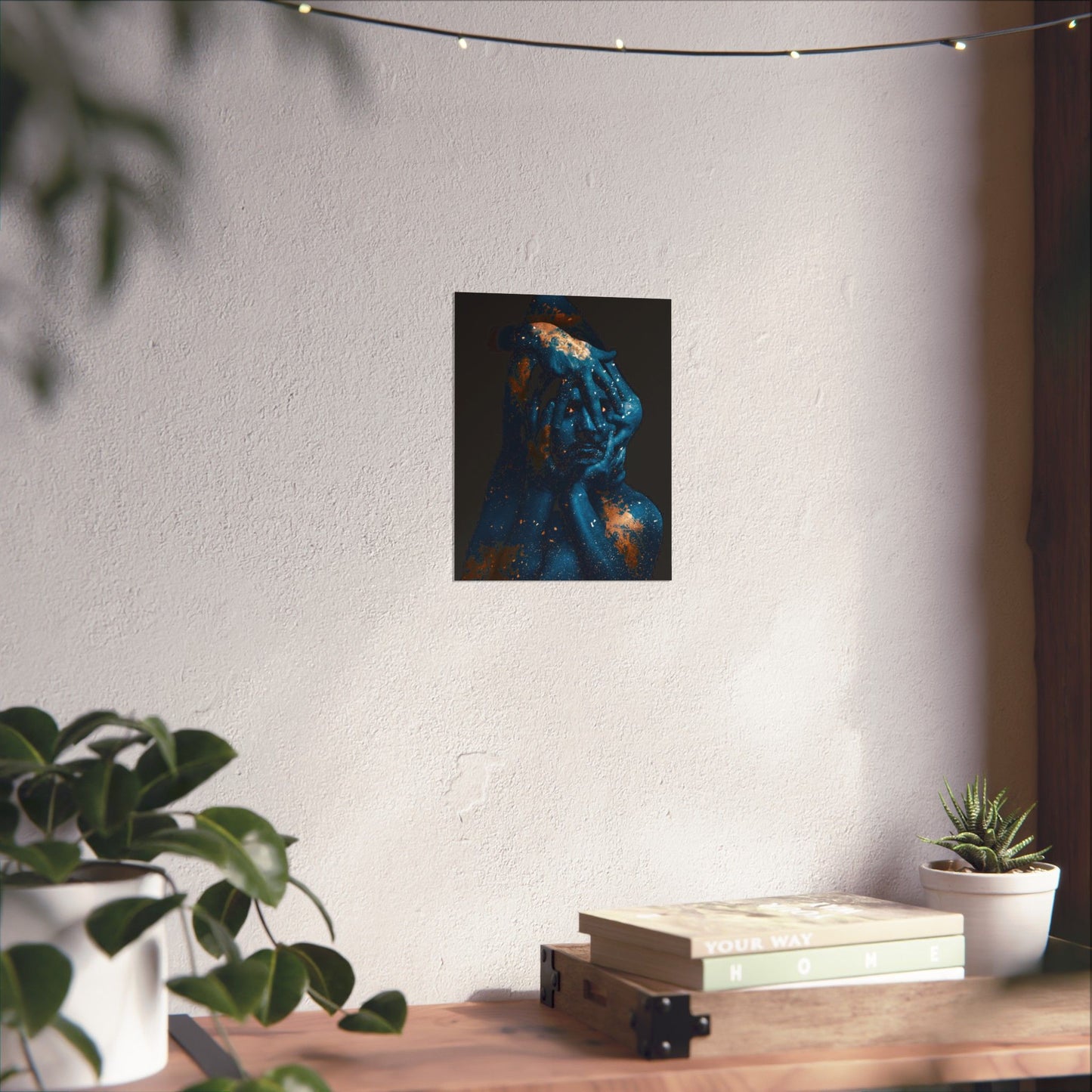 Framed artwork on a wall above a wooden table with plants and books.