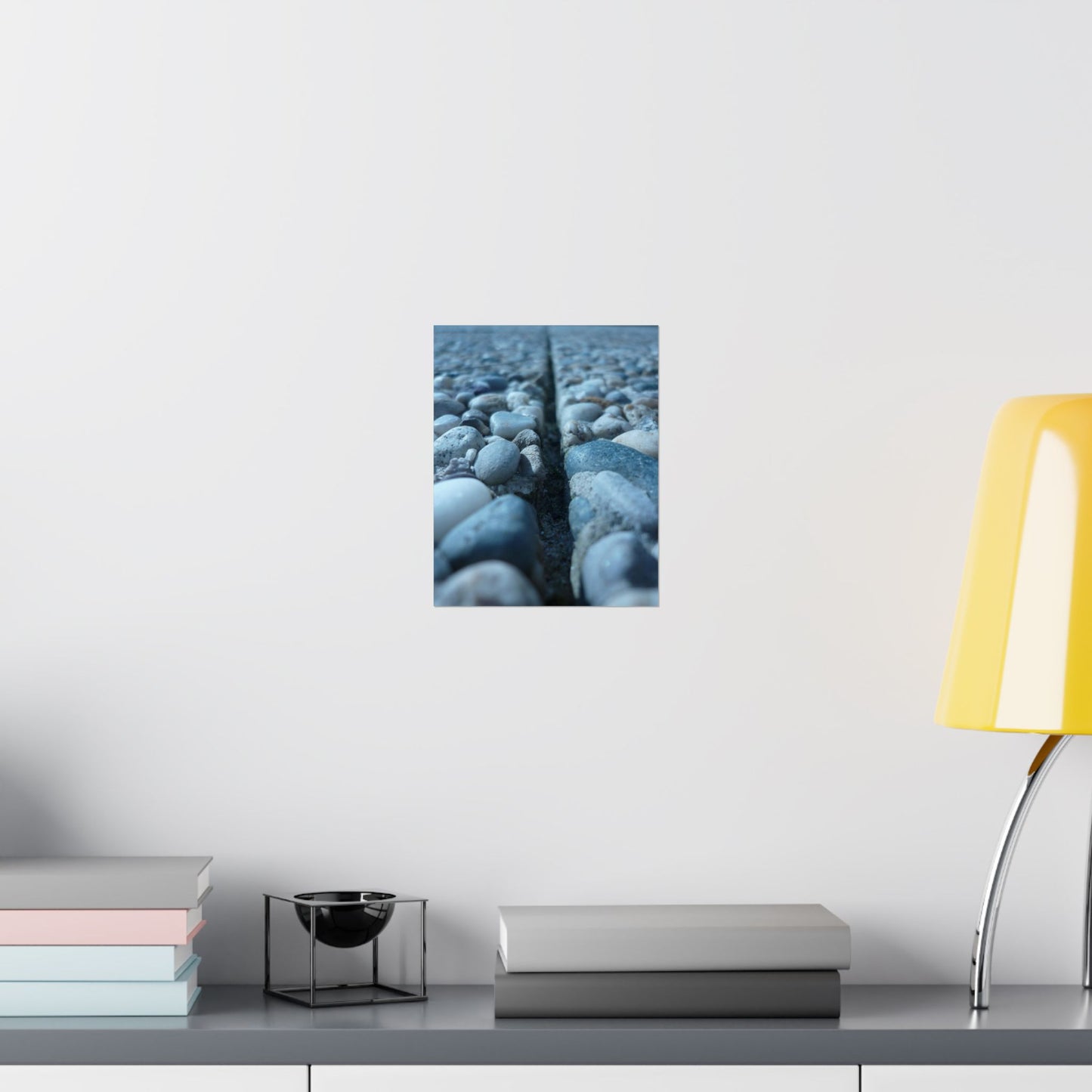 Wall art of pebbles on a white wall above a shelf with books and a lamp.