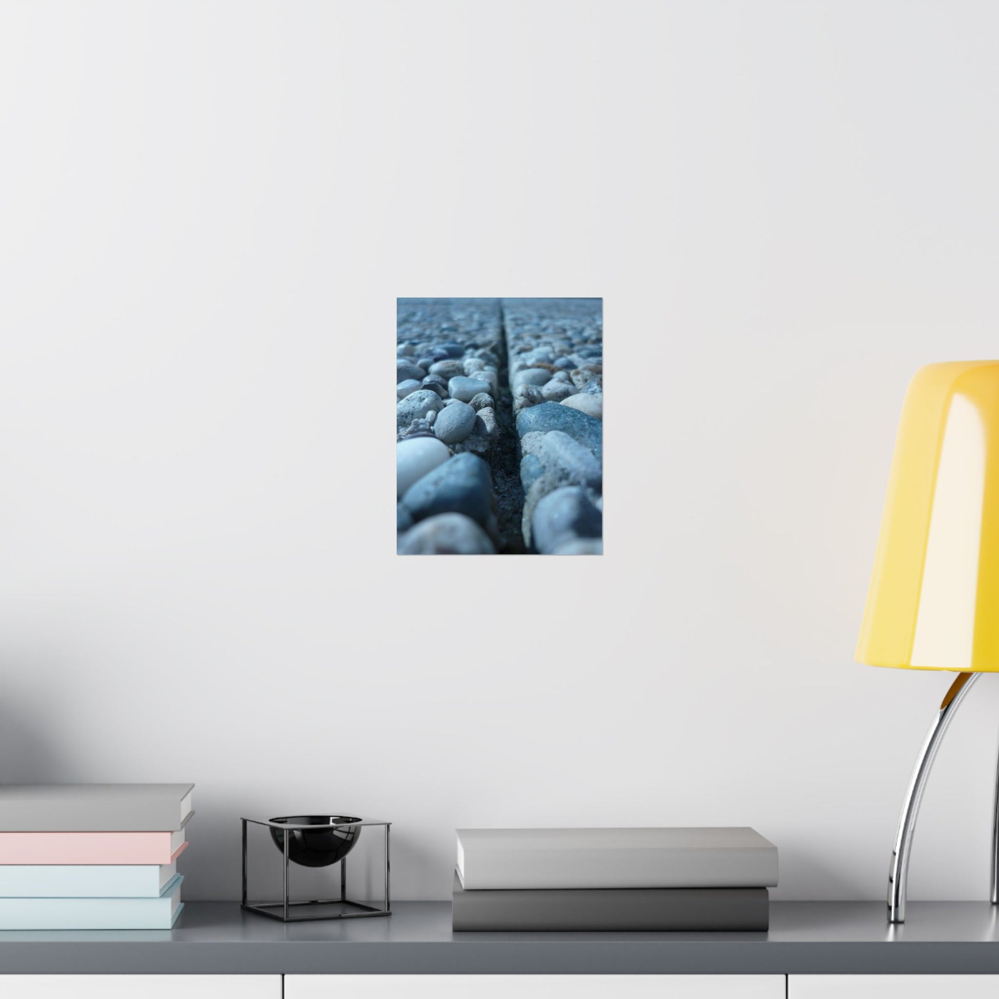 Wall art of pebbles on a white wall above a shelf with books and a lamp.