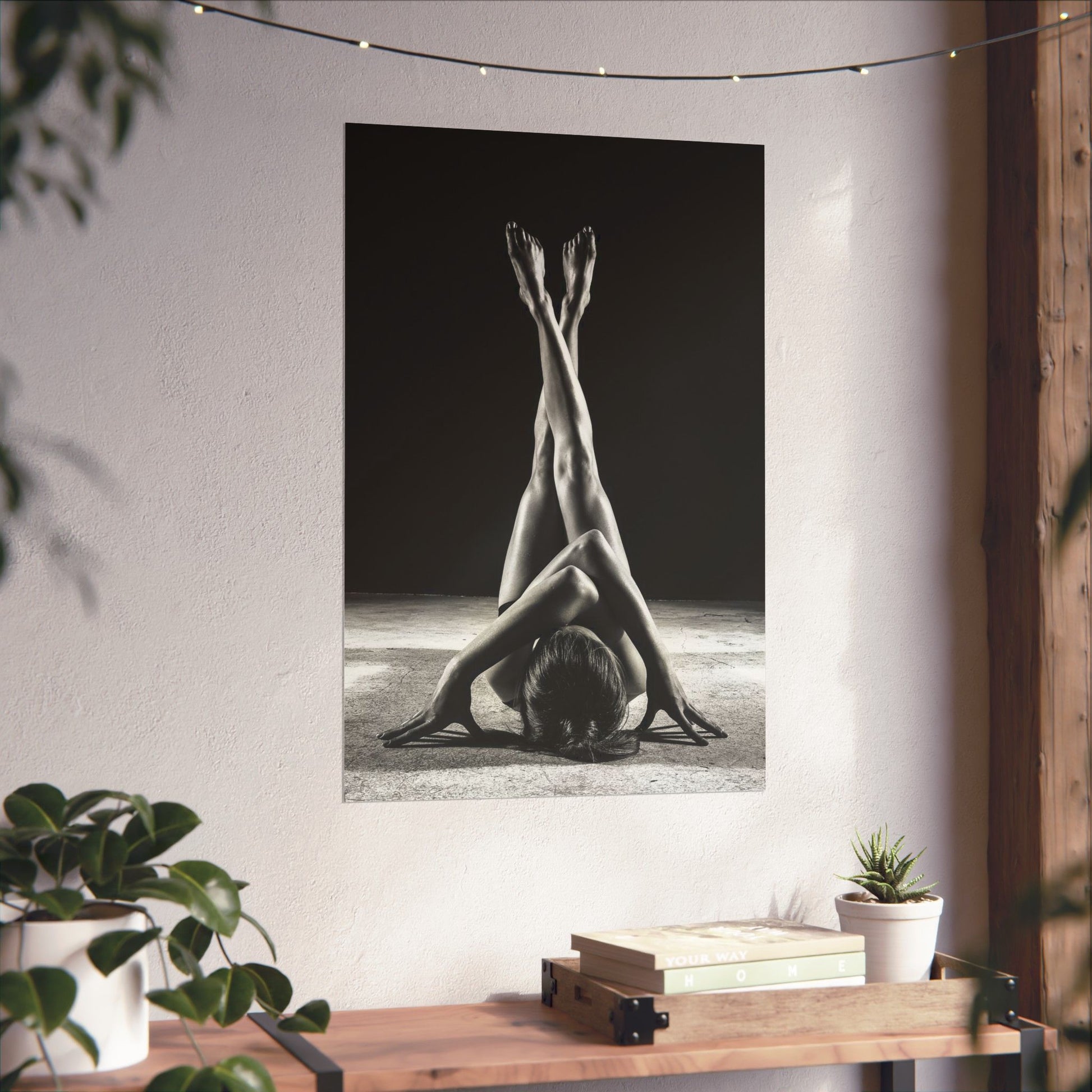 Black and white photograph of a person in a yoga pose on a wall in a room with plants and books.