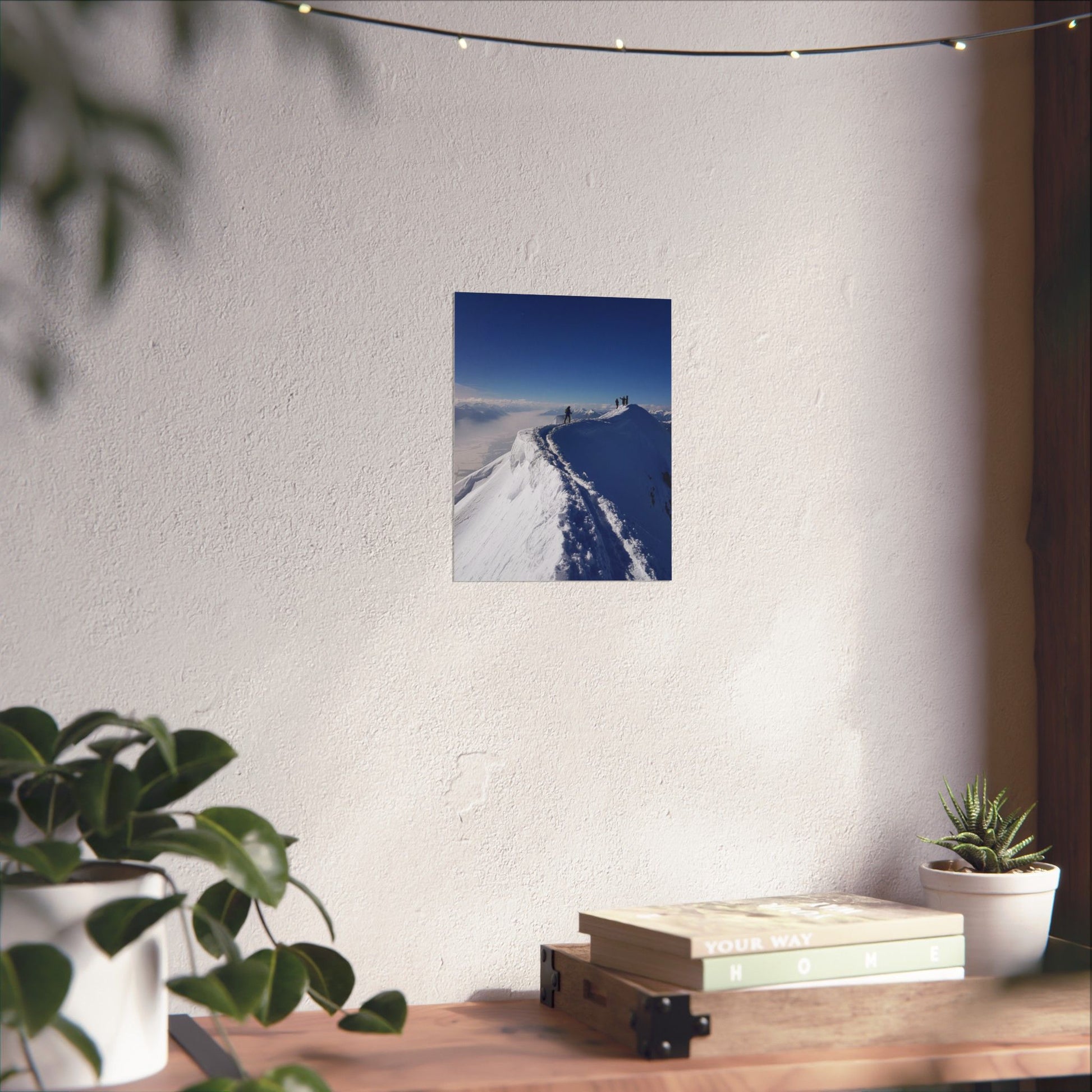 Poster of a snowy landscape on a white wall above a wooden desk with plants and books.