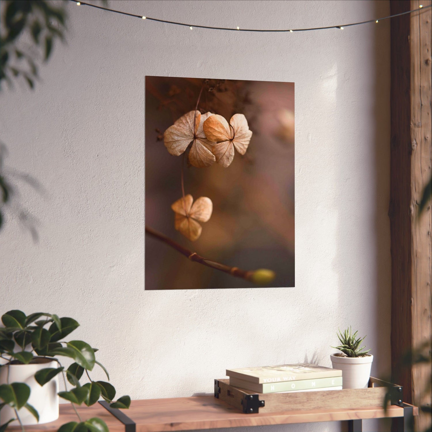 Art print of dried flowers on a wall with a wooden table and plants below