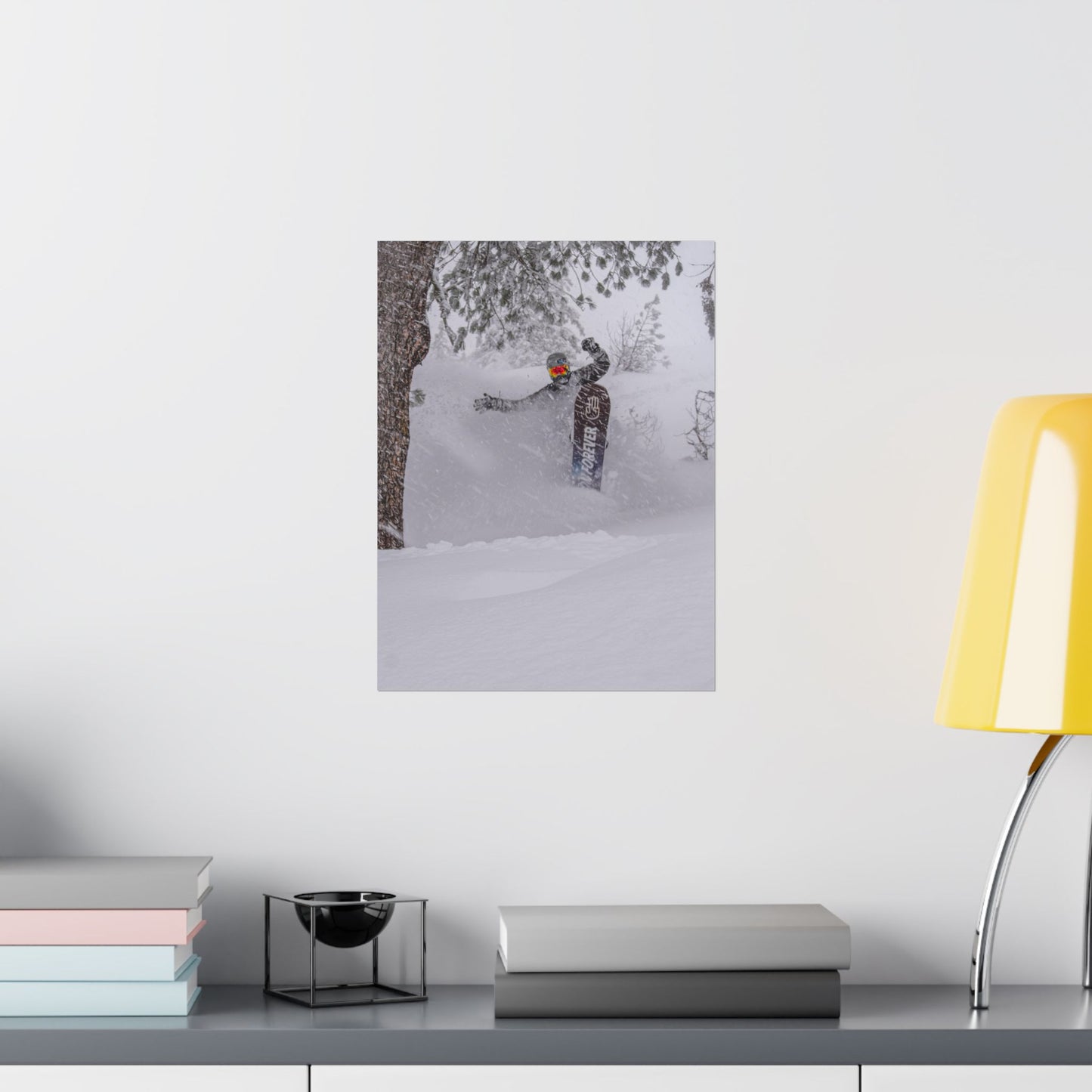 Poster of a person skiing on a snowy mountain wall-mounted above a desk with books and a lamp.