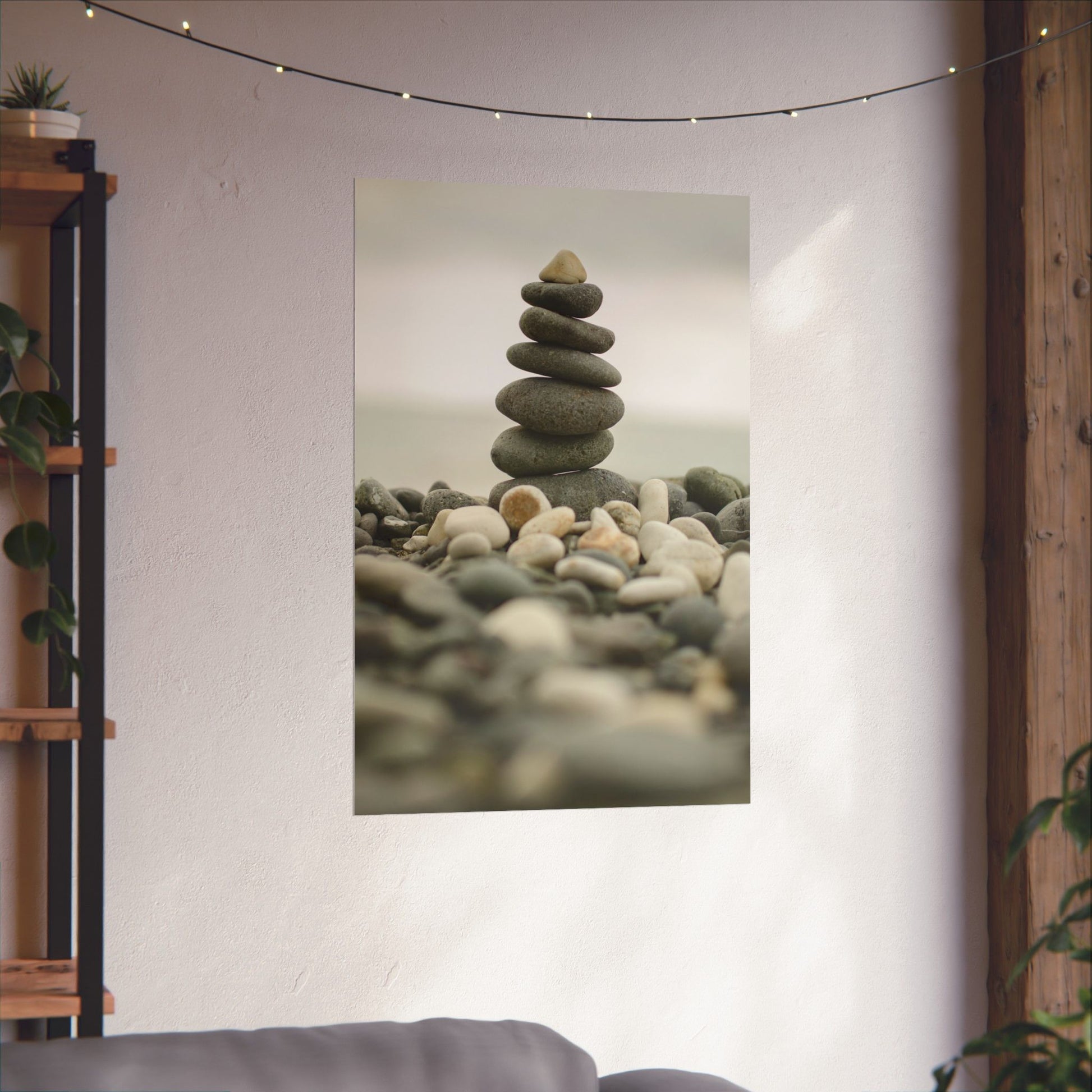 Poster of stacked stones on a wall in a room with plants and a shelf.